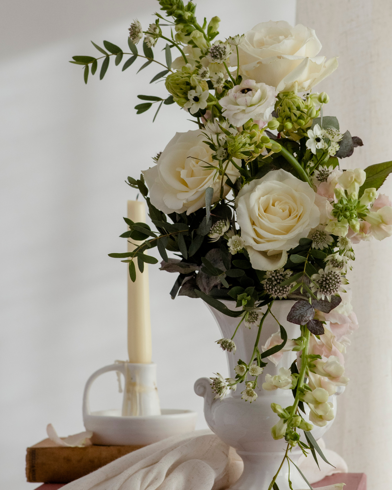 A white Rococo style vase filled with a draping floral display of roses and ranunculus for a wedding