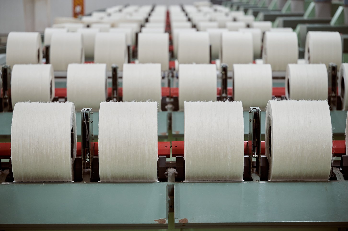 Rows of large white spools of thread on industrial conveyor rollers in a textile factory.