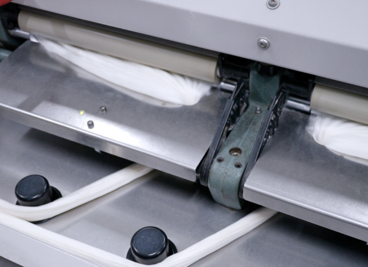 Close-up of an industrial machine processing white fabric or material on a metal conveyor system.