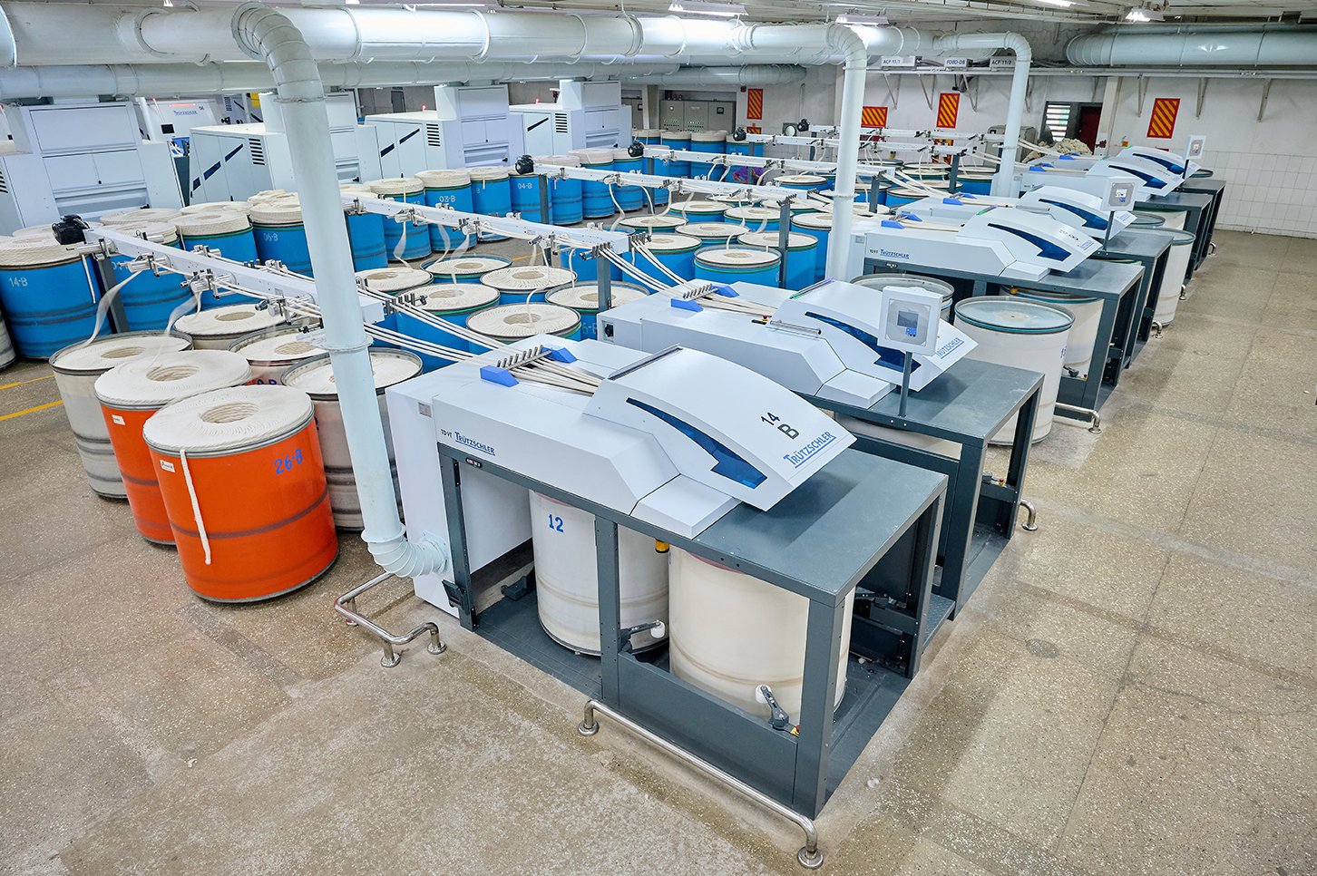 Industrial laundry room with multiple industrial-sized washing machines and large blue and orange open-top drums.