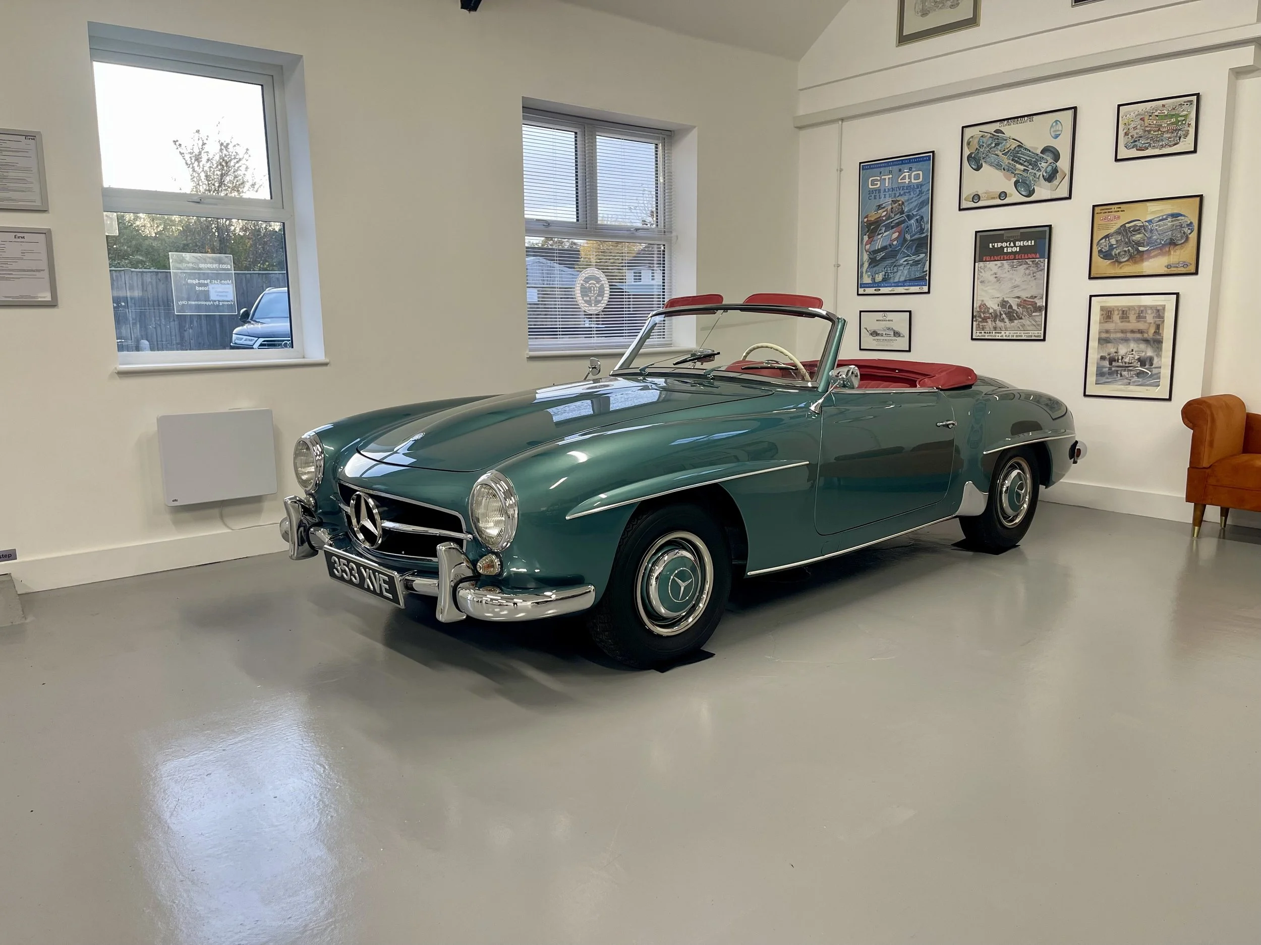 A vintage green Mercedes-Benz convertible car with a red interior on display indoors, with framed automotive posters on the wall behind it.