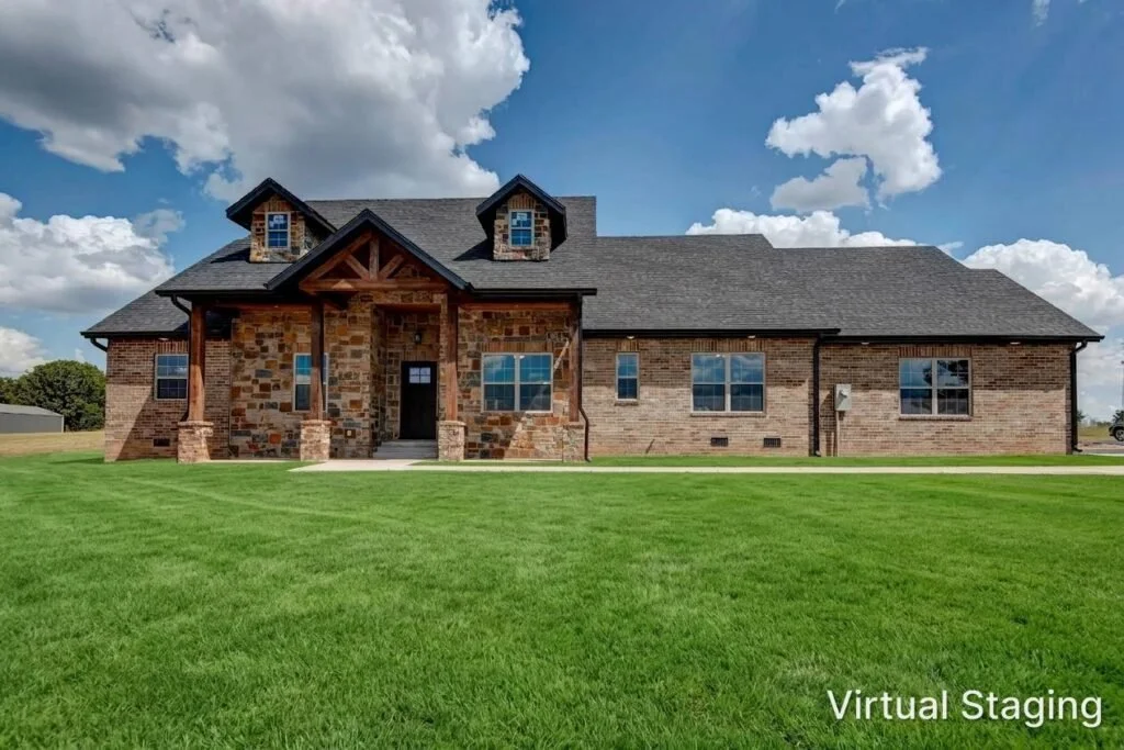 A large brick house with a stone and wood front porch, multiple windows, and a dark roof. The house is surrounded by a well-maintained grassy lawn under a partly cloudy sky. The bottom right corner has the text 'Virtual Staging'.