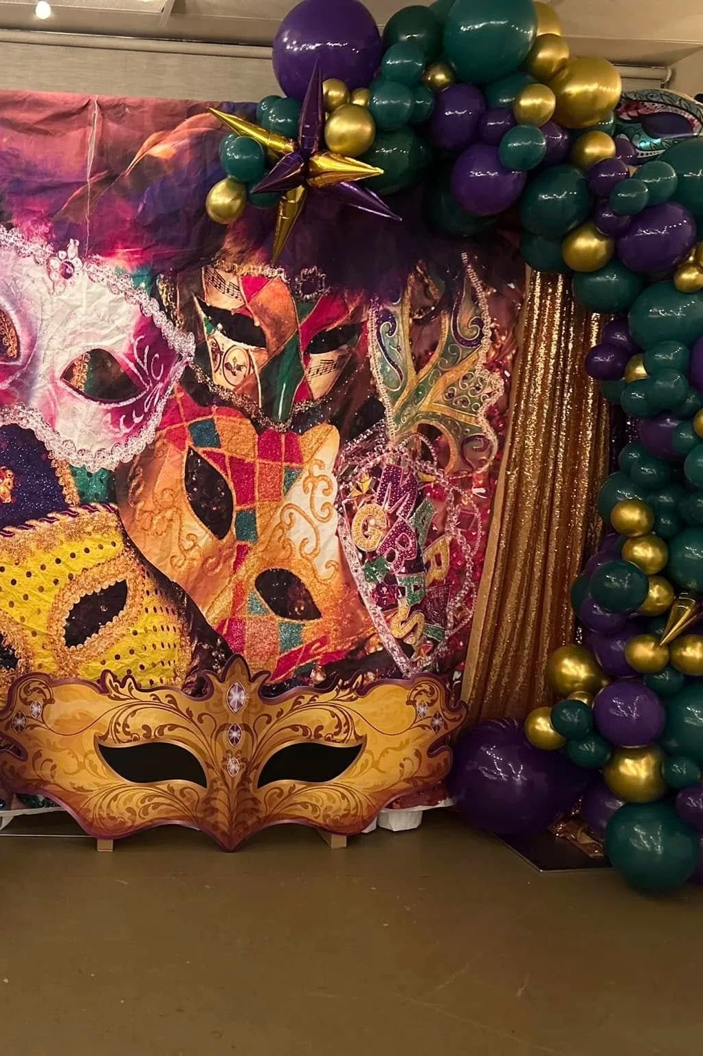 Colorful Mardi Gras masks, gold, purple, and green balloons, and gold curtain decorations at a party or celebration.