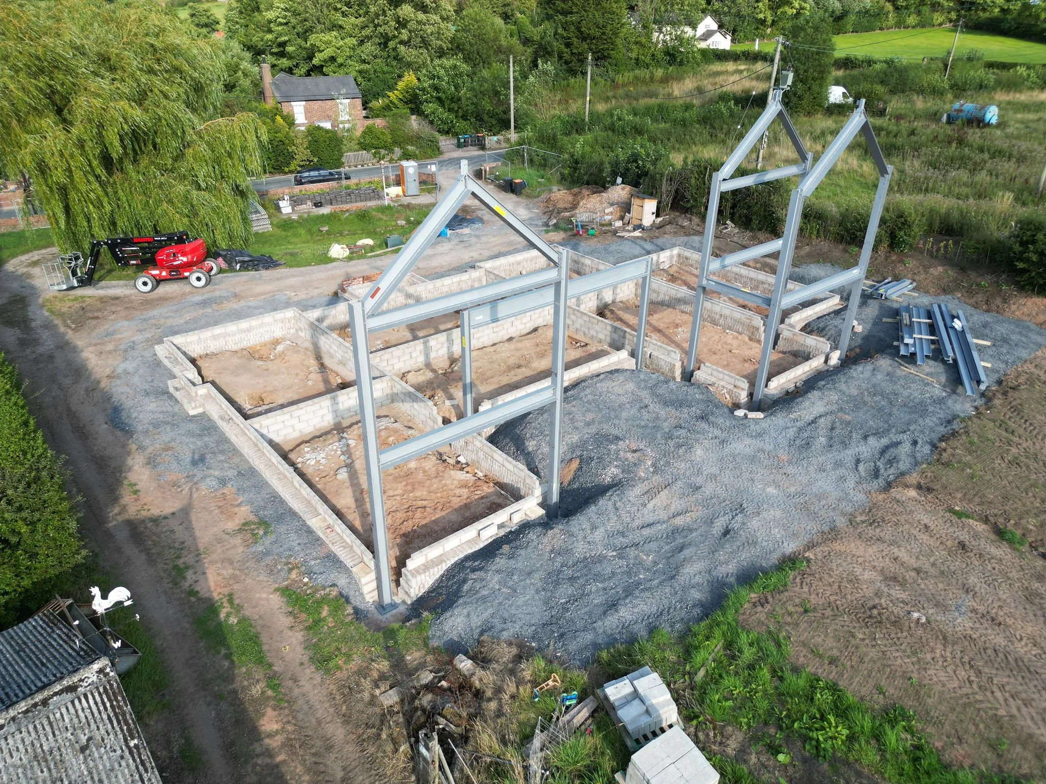 A construction site with building foundation and steel framing in progress surrounded by greenery and rural landscape.