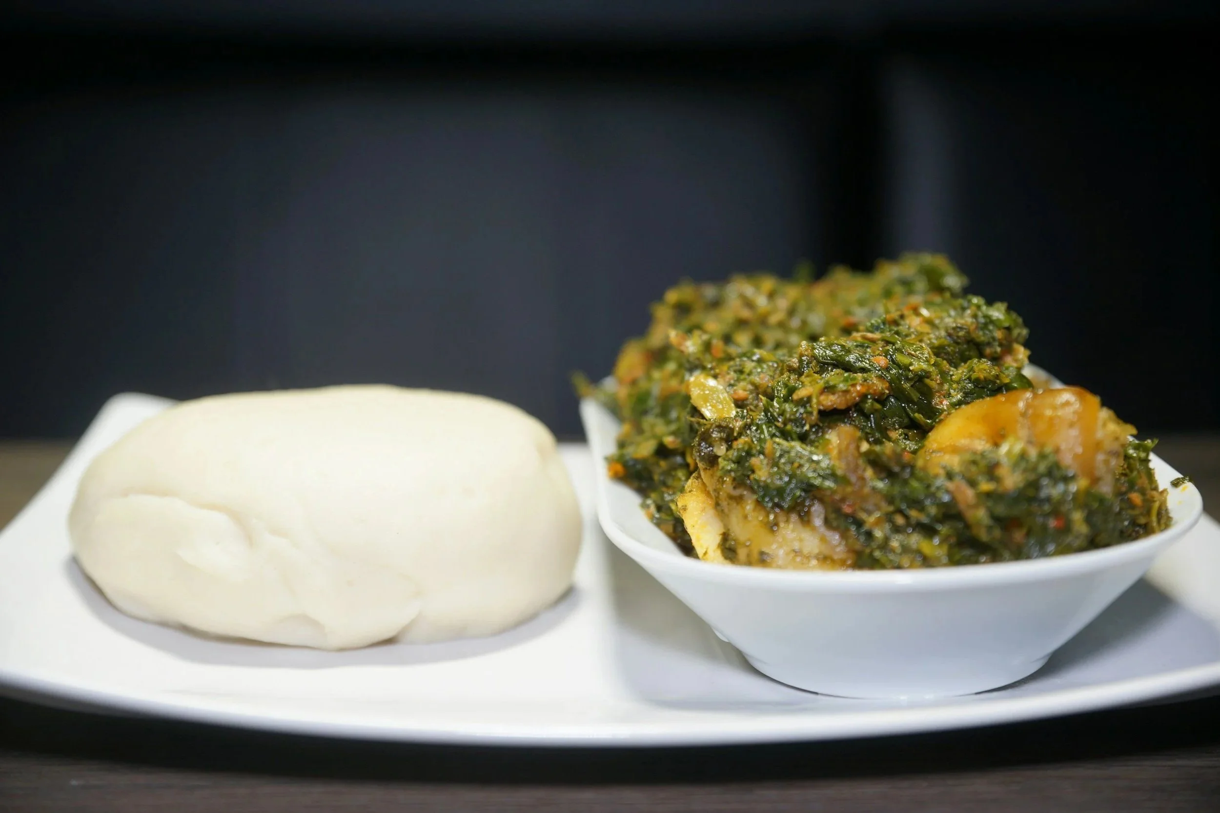A traditional plate of poundo (iyan) served with a bowl of traditional spinach (efo riro) stew.