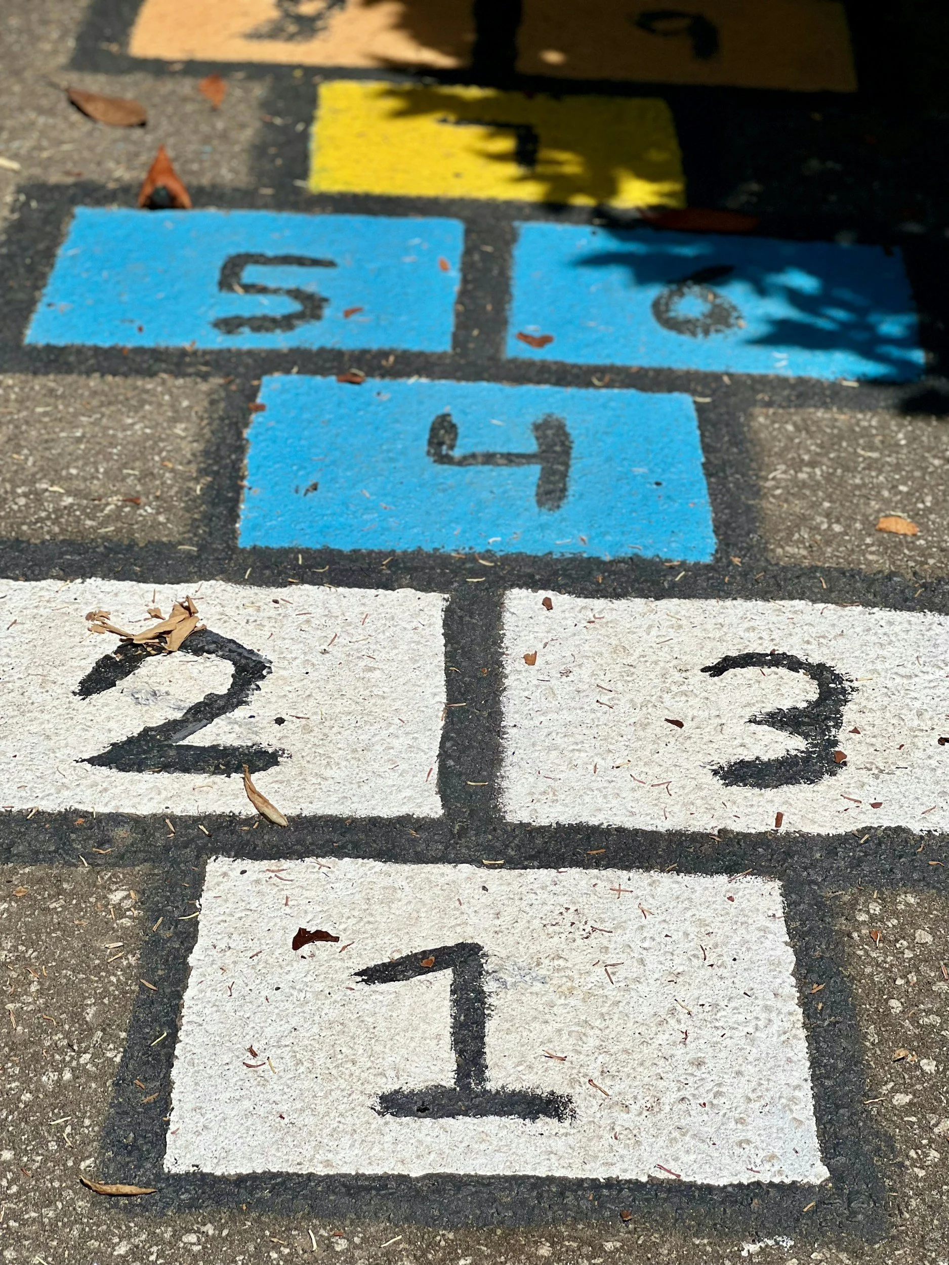 Colorful hopscotch grid painted on pavement with numbered boxes from 1 to 4, and two colored boxes numbered 5 and 6 at the top.