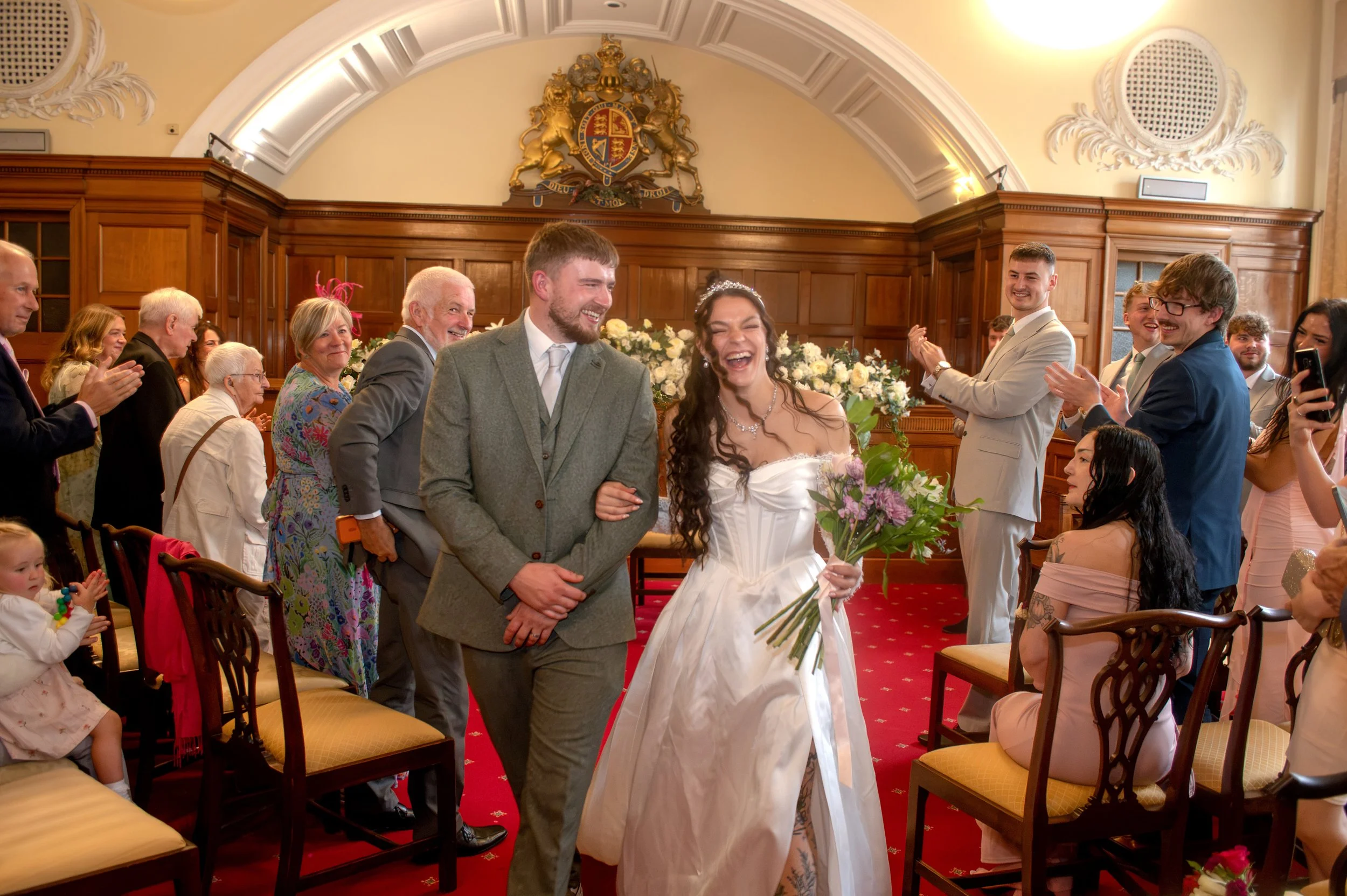 A bride and groom walking down the aisle while guests clap and cheer in a decorated wedding venue.