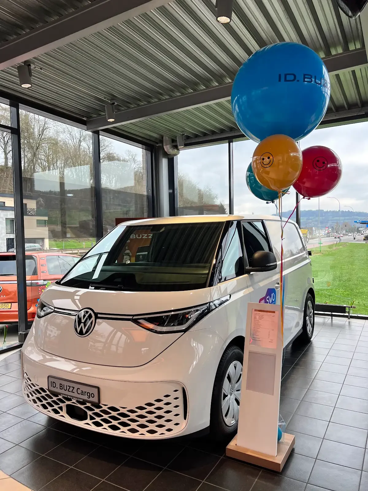Balloon arch in white, blue, and silver decor with a white curtain backdrop and three white pedestals, set up for a celebration.