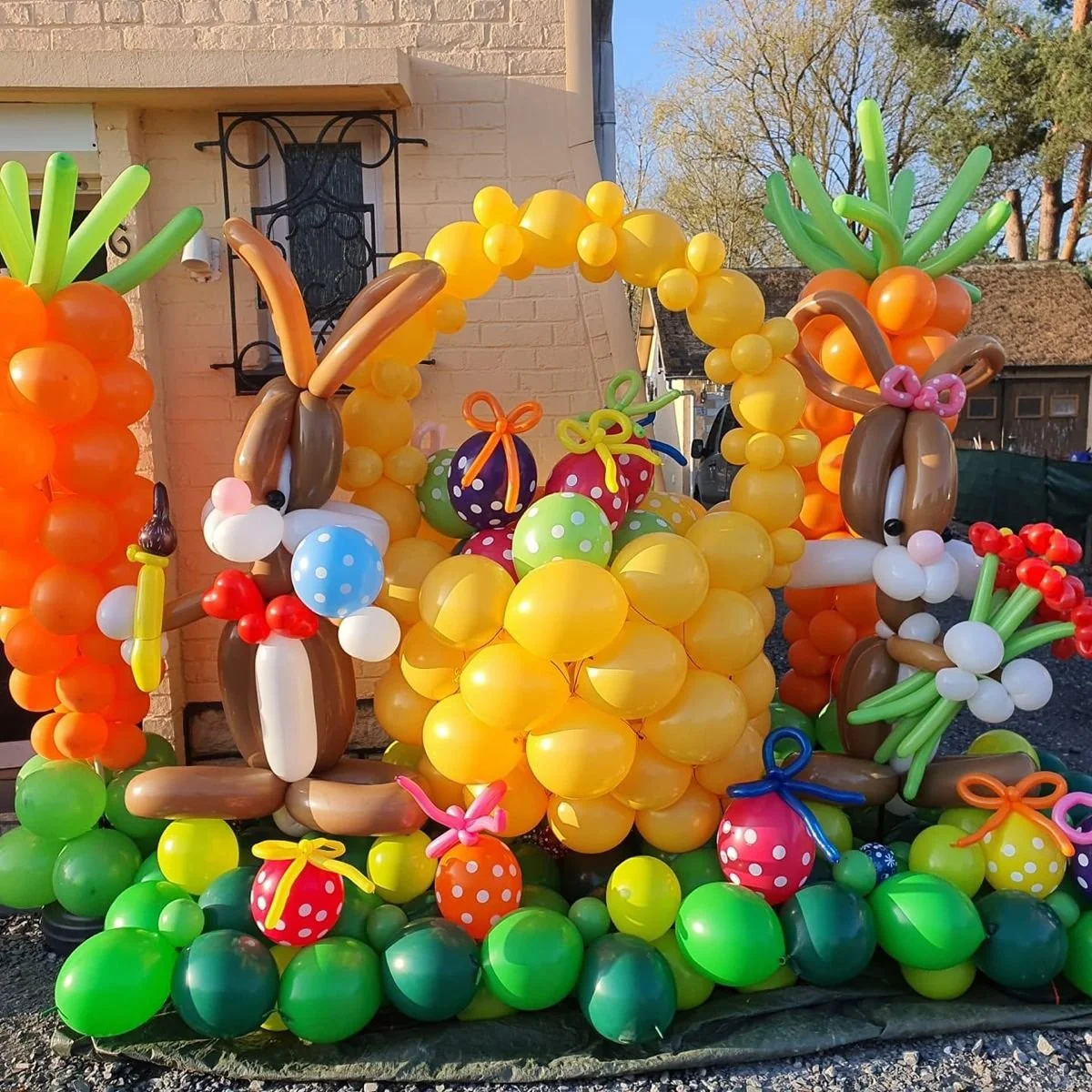 Balloon decoration featuring a large yellow arch, two balloon rabbits with long ears, and various colorful balloons resembling eggs and presents.