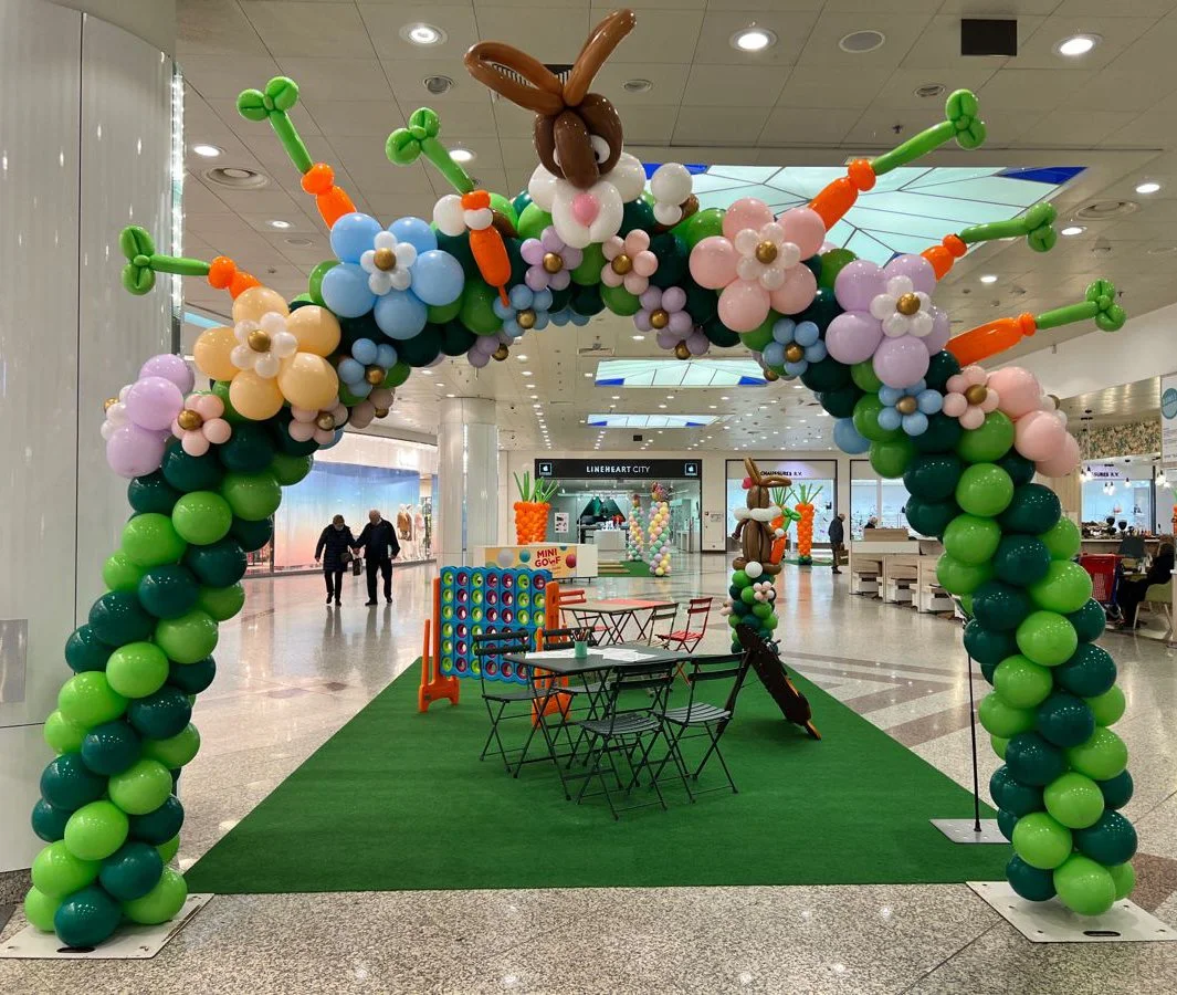 Colorful balloon arch decorated with flowers, carrots, and bunnies in a shopping mall.