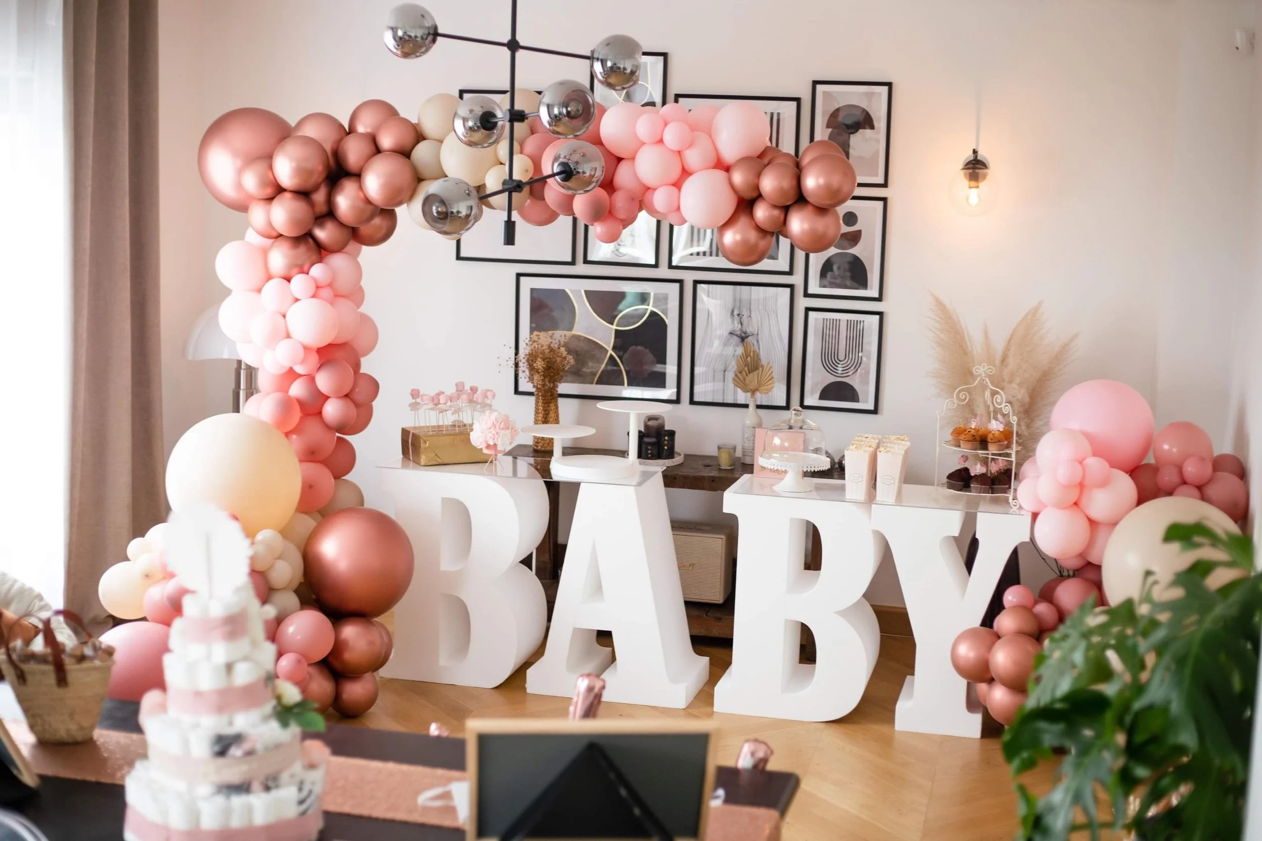 A decorative arrangement of plush teddy bears, white and beige balloons, and a small stuffed unicorn, creating a soft, cozy scene.