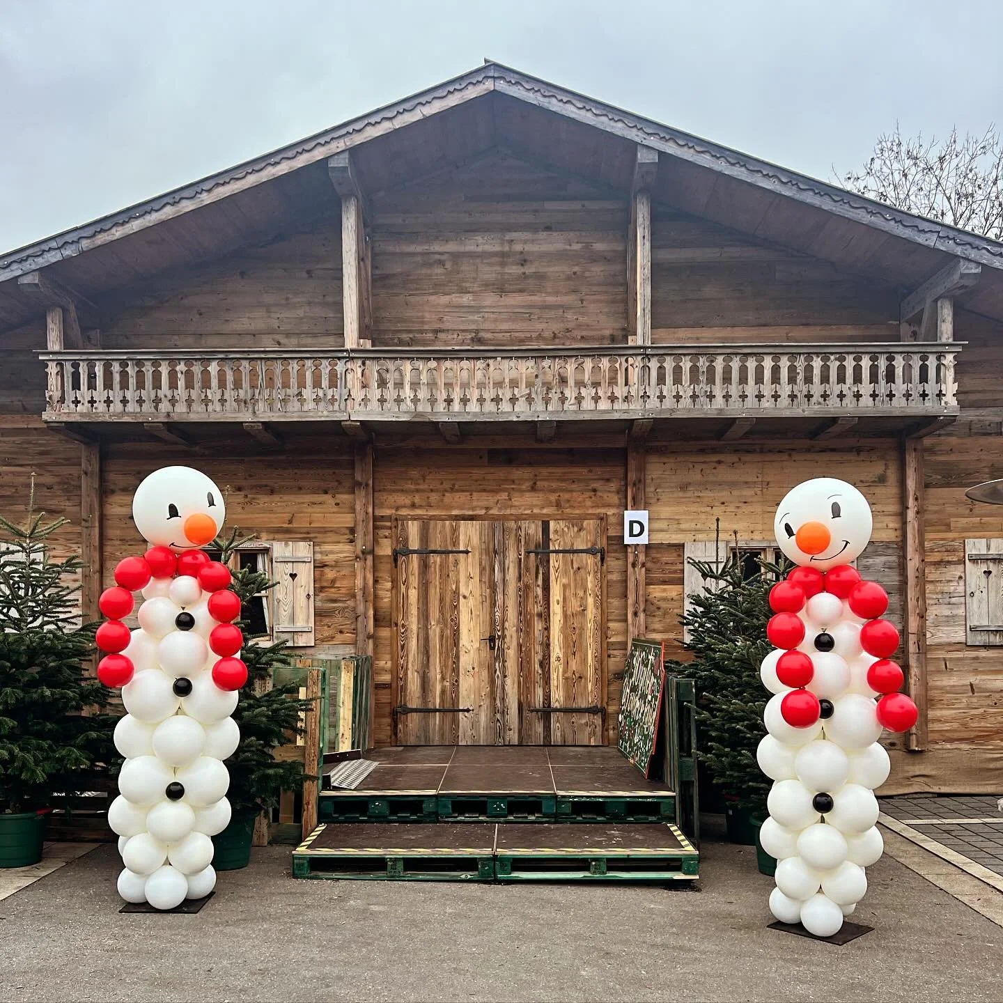 Christmas decorations with two balloon snowmen flanking a wooden barn entrance.