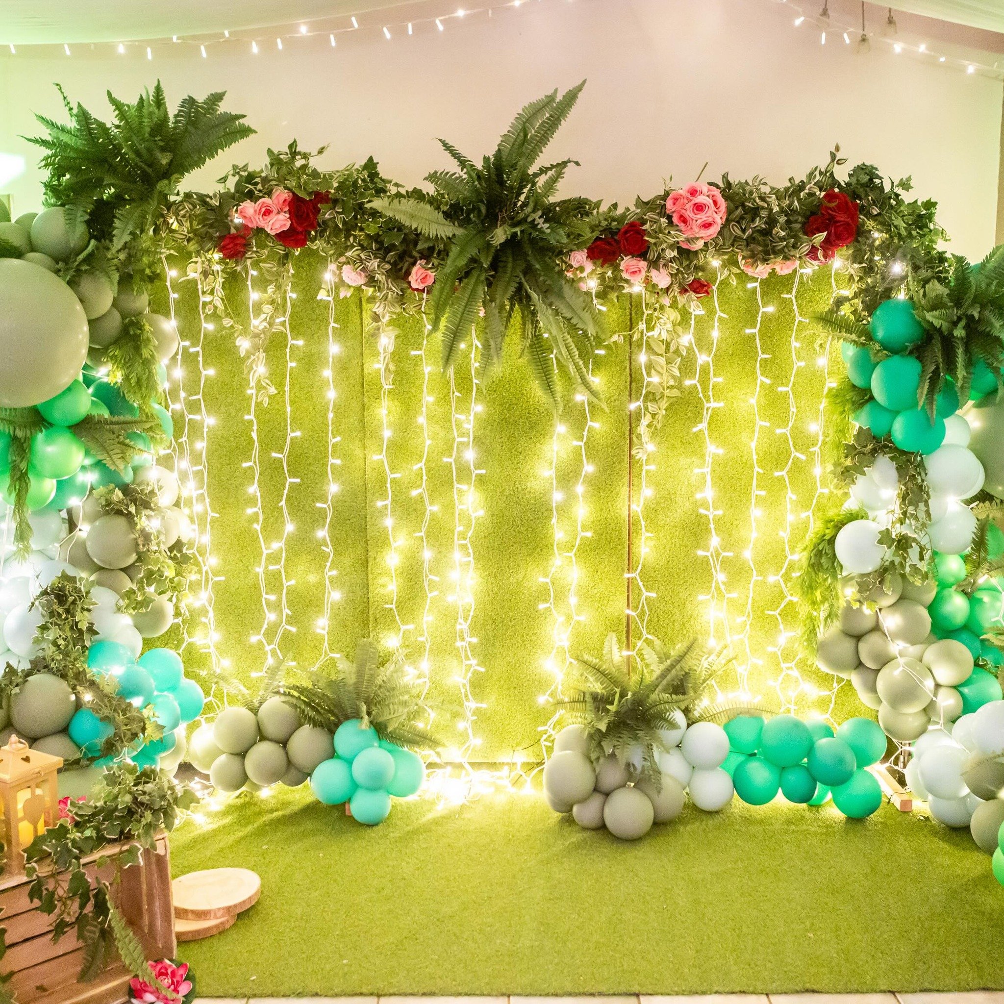 Decorative backdrop with greenery, flowers, and fairy lights for a celebration or event.