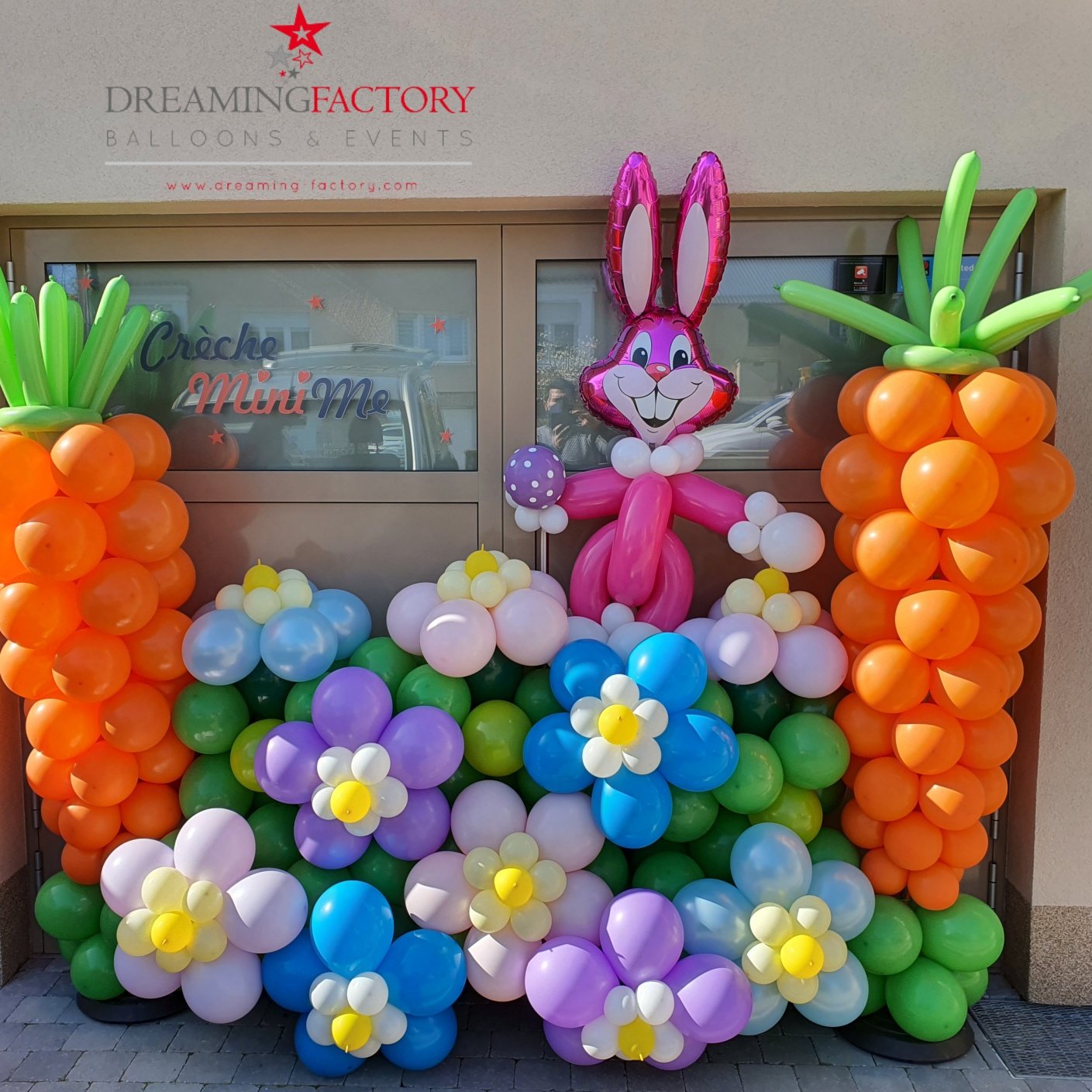 Decorative display of colorful balloons including carrots, flowers, and a pink bunny, with a sign for Dreaming Factory Balloon & Events.