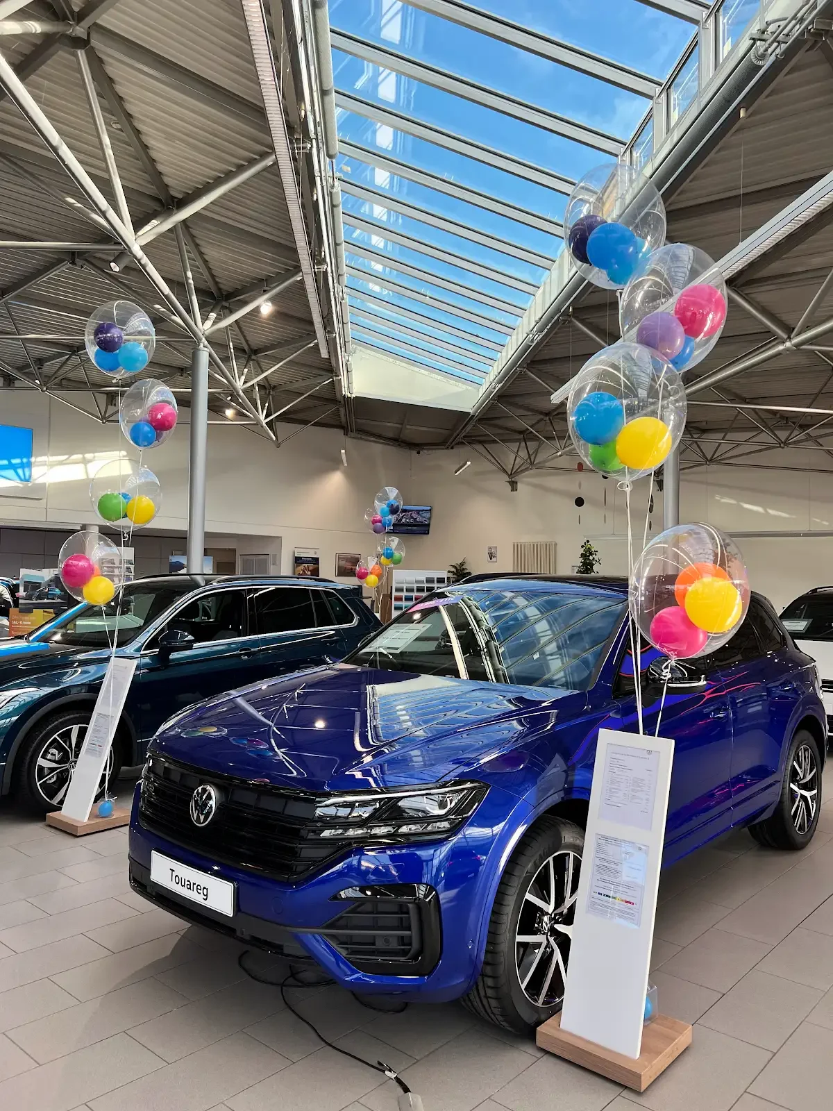 A balloon arch and display with pink, blue, and white balloons and blocks with letters B, A, B, Y arranged vertically, set outdoors on grass surrounded by trees.