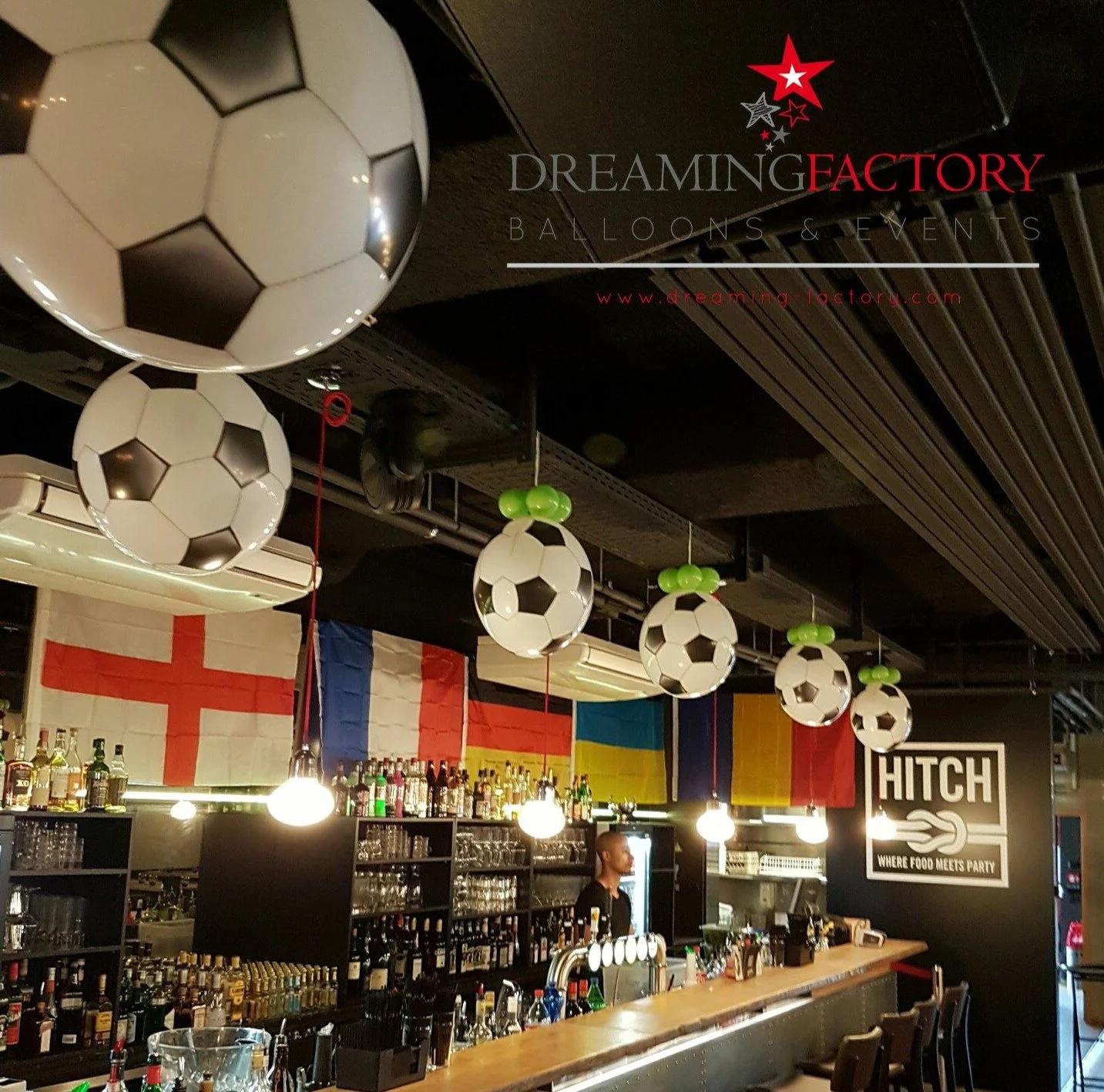 Bar area decorated with soccer ball hanging lights and international flags, including England, France, and Ukraine, at a party venue.