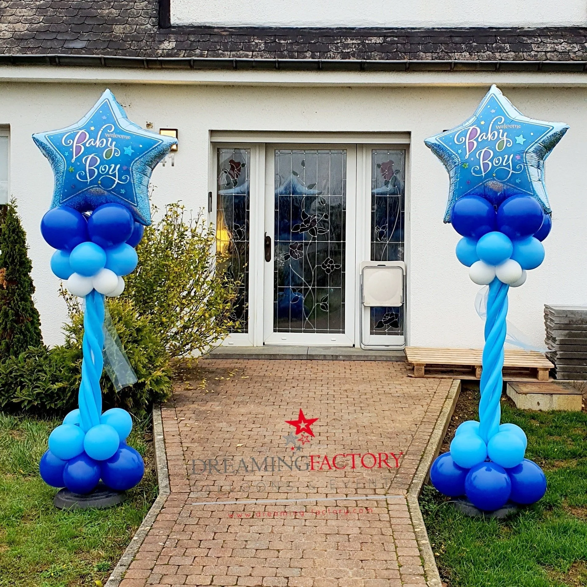 Blue balloon arrangements with star-shaped balloons that say "Welcome Baby Boy" on each side of a front door of a house.