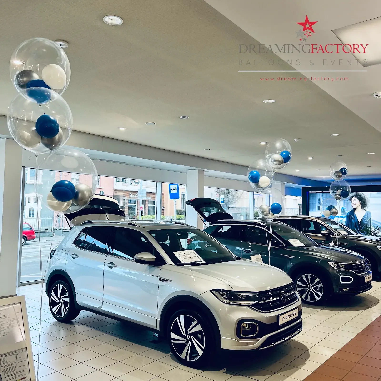 Decorative balloon arrangement with pink, blue, and gold balloons, including a large gold crescent moon helium balloon, set against a wooden gate backdrop. A white display rack with balloons and birthday letters is also visible.
