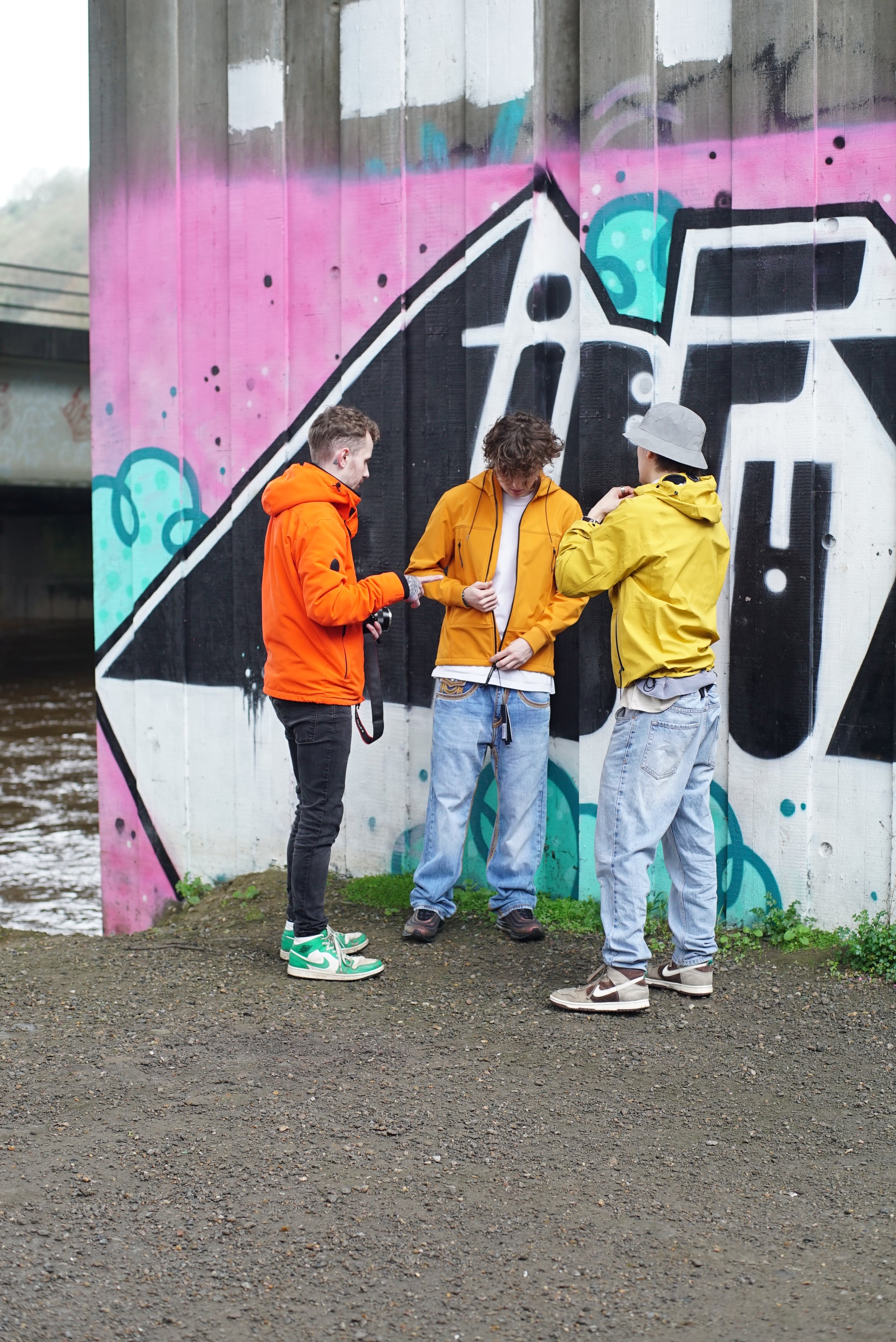 A Photographer speaks to two models wearing Orange and Yellow CP Company Jackets.