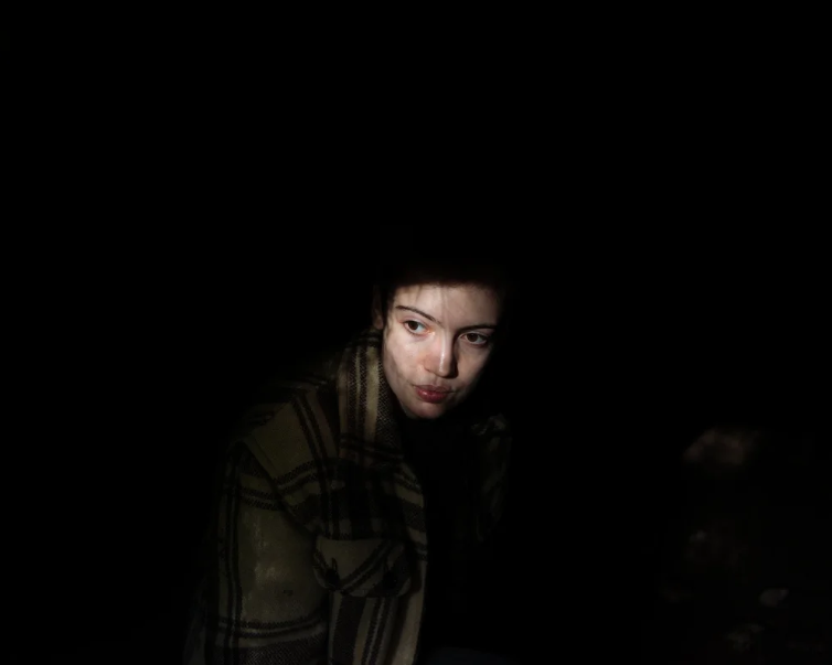 Colour photograph of Robert Darch's The Moor showing a woman looking to the left of frame in a striped jacket in a dark environment.