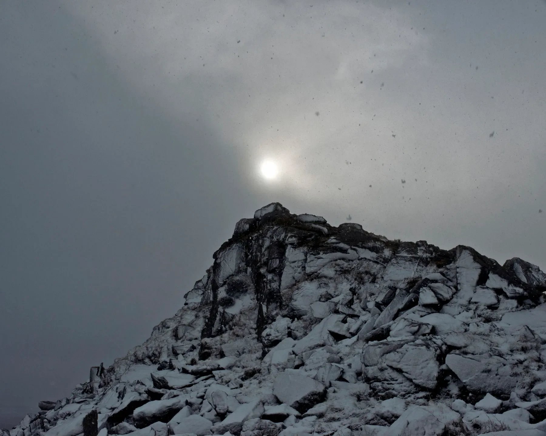 Photograph of a snow capped ridge on Dartmoor National Park. Birds can be seen flying and light in the backdrop