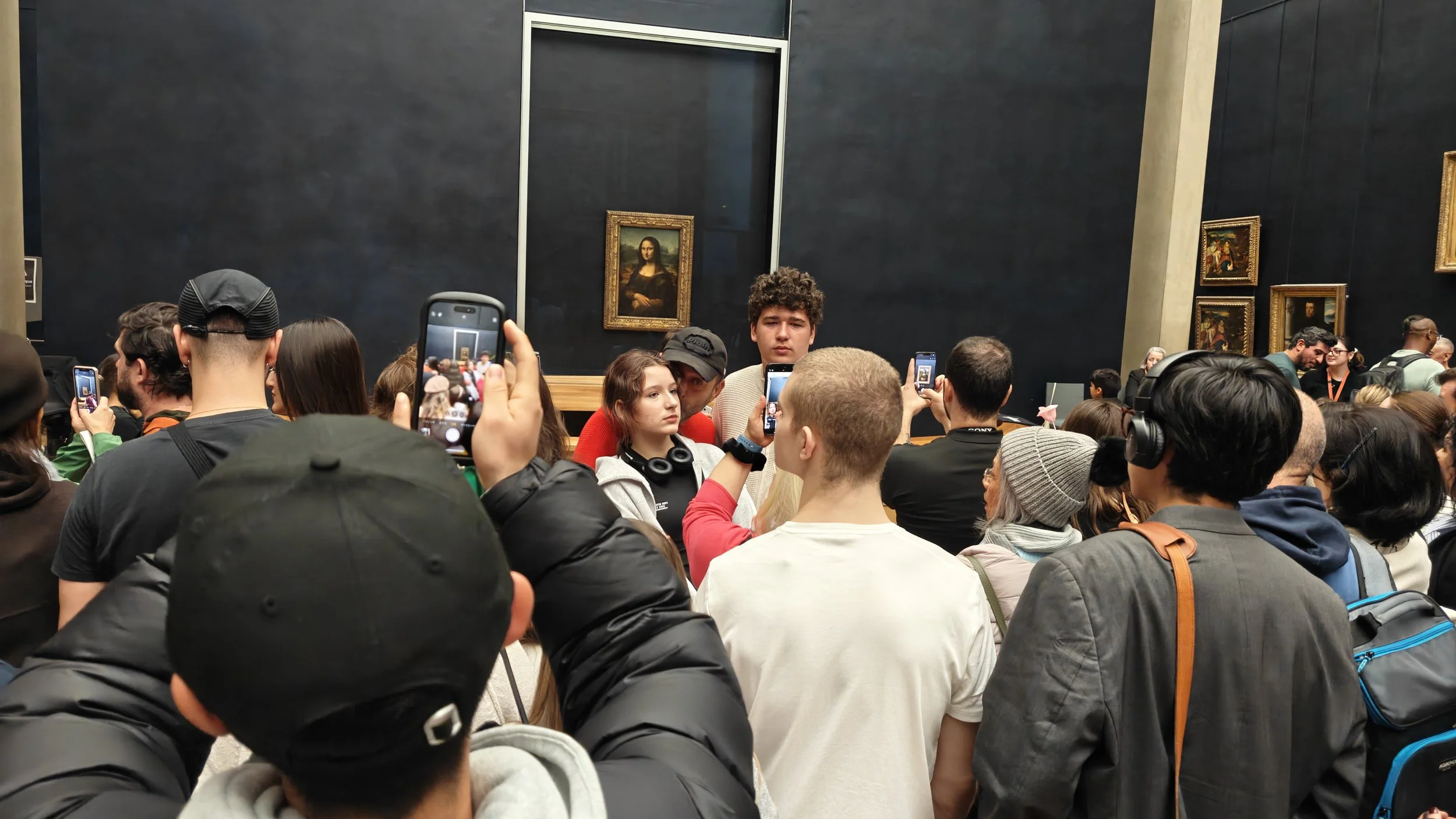 Crowds of people with smartphones photograph the Mona Lisa at The Louvre, Paris.
