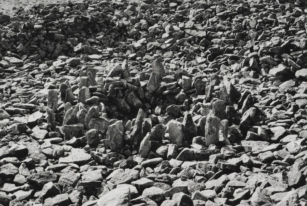 Black and white photograph of stones on a cairn from Richard Long on rocky terrain.