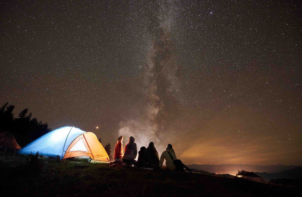 A group of people gathered around a campfire, enjoying the warmth and light under a starry night sky.