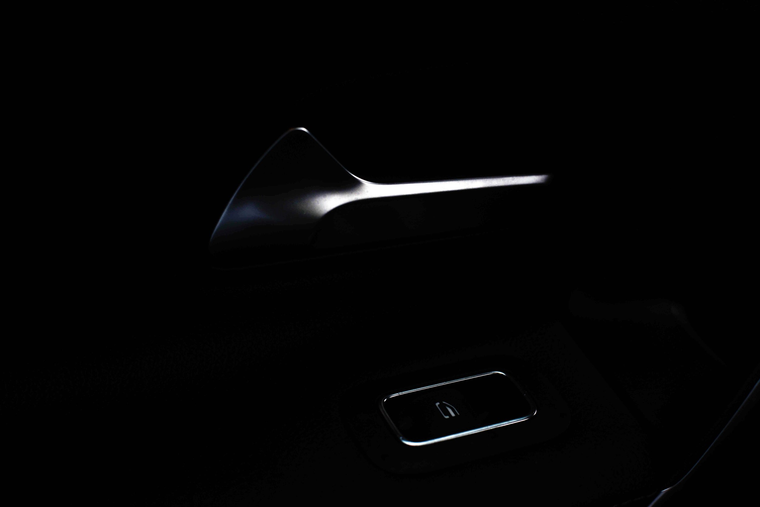 Close-up of an illuminated car door handle and window control button in a dark interior, creating a sleek and modern ambiance