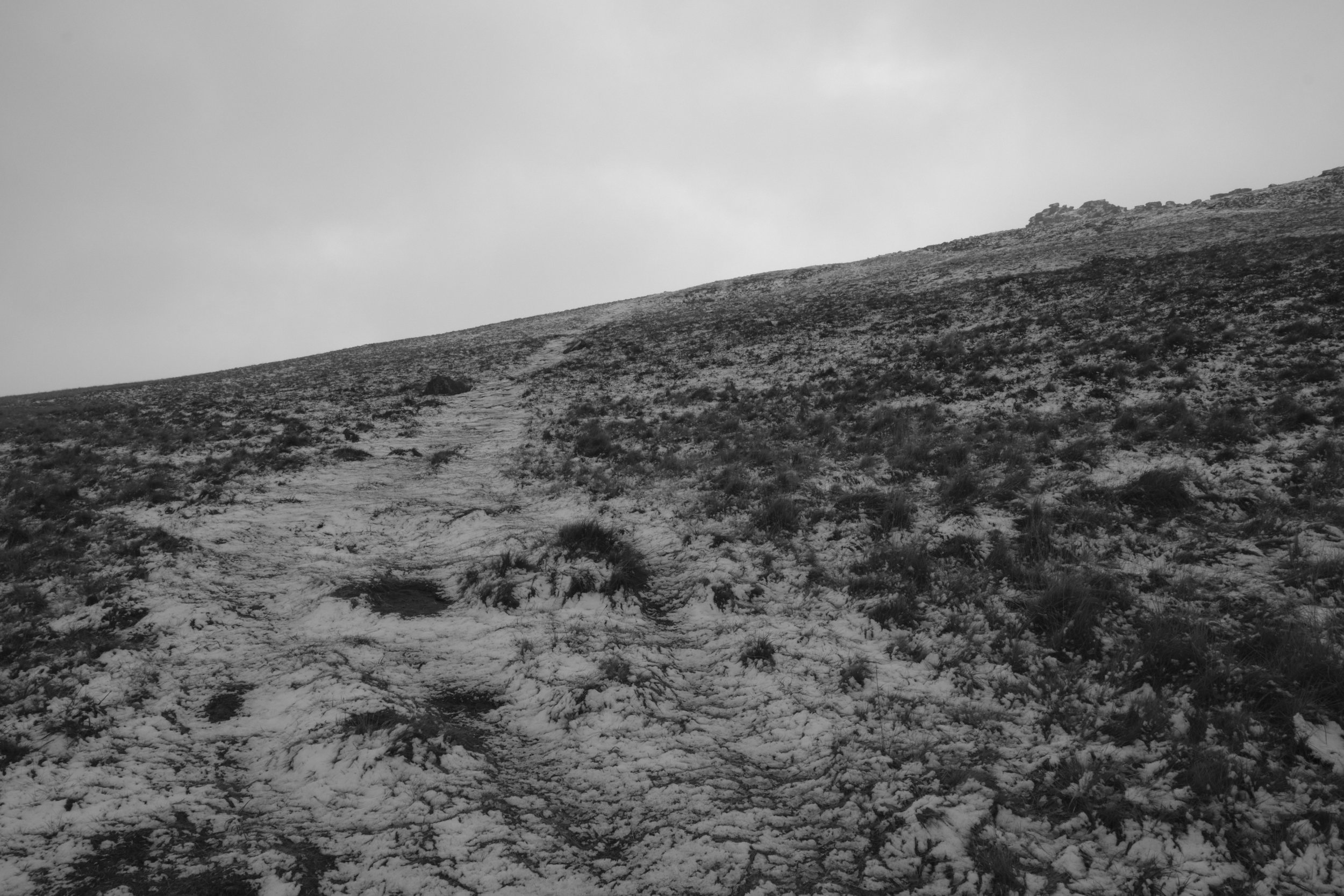 Snow-covered trail on a hillside under an overcast sky.