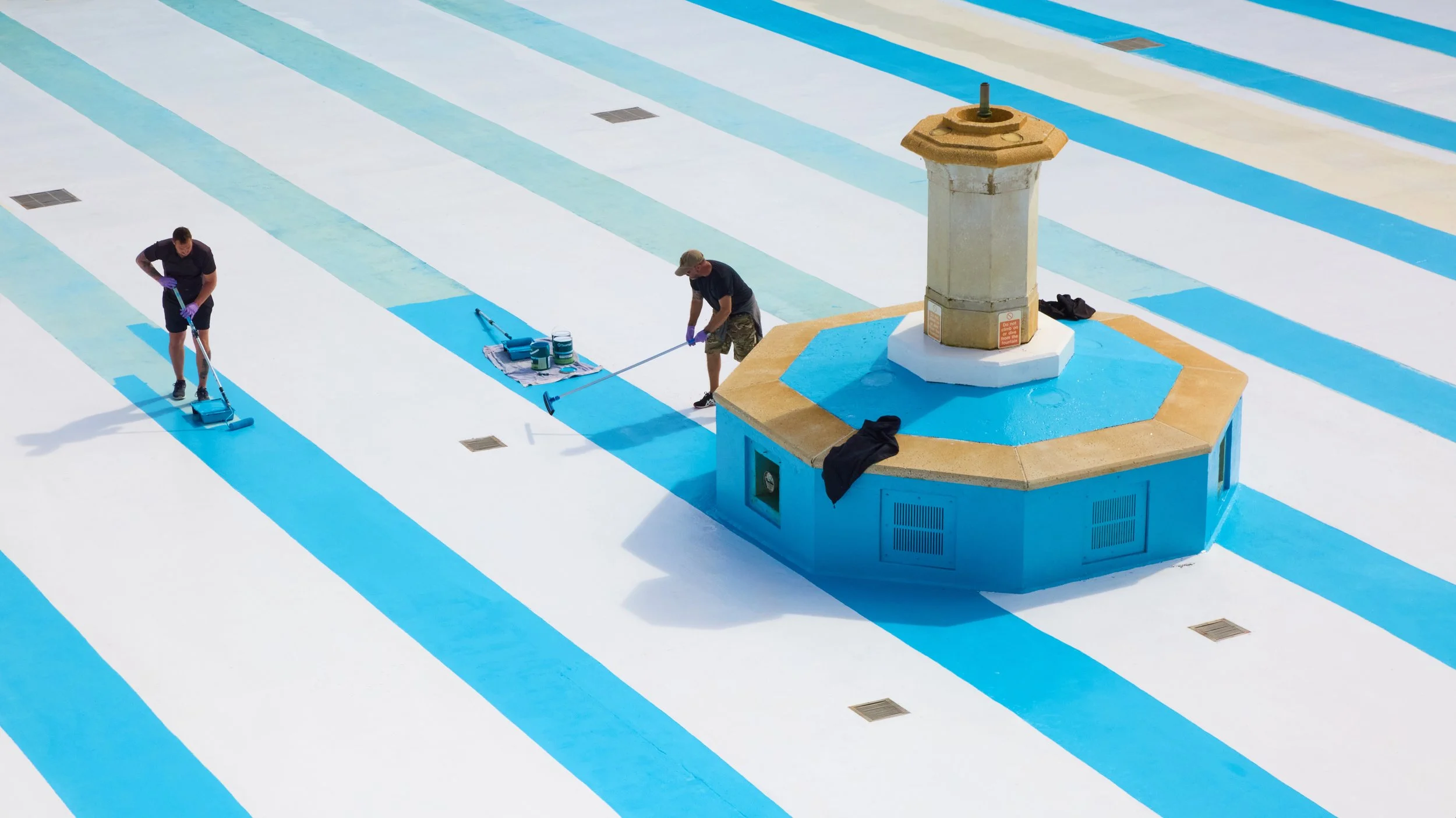 Photograph of two workers repainting the base of Tinside Lide by hand.