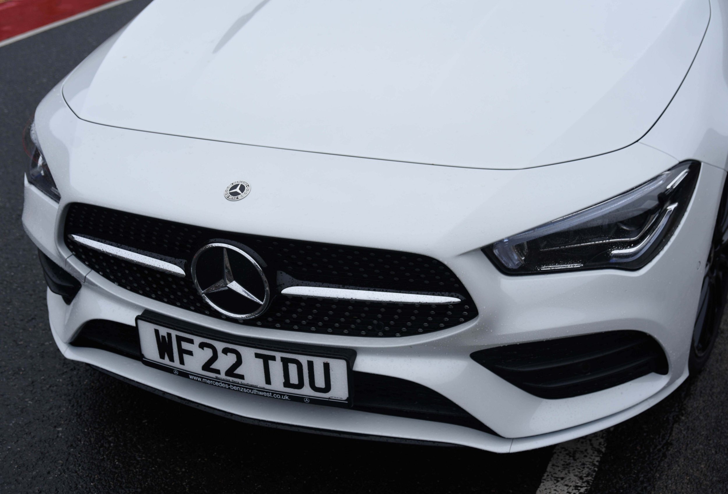 Close-up of a white Mercedes-Benz car front, featuring the iconic emblem on a sleek grille and sharp headlights.