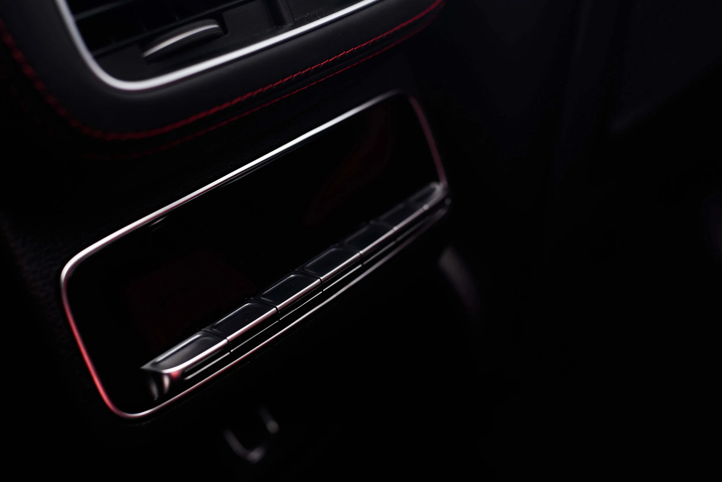 Close-up of a sleek car interior vent with red stitching detail and chrome accents. The image conveys a sense of luxury and modern design.