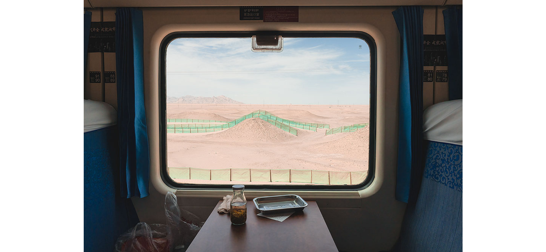 A train window frames a sweeping view of the arid desert terrain, showcasing its natural beauty. A scenic view of the vast desert stretches out under a clear blue sky.
