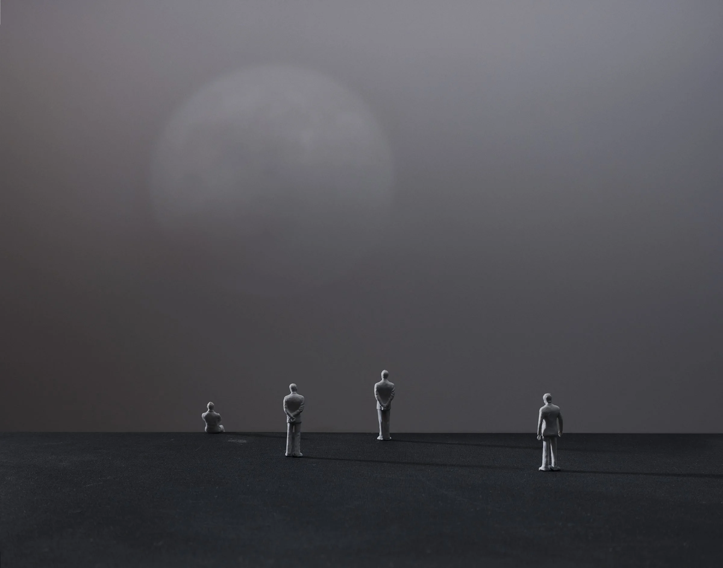Photograph from Nadav Kander's The Pause project featuring four toy figures looking against a grey backdrop on a black surface