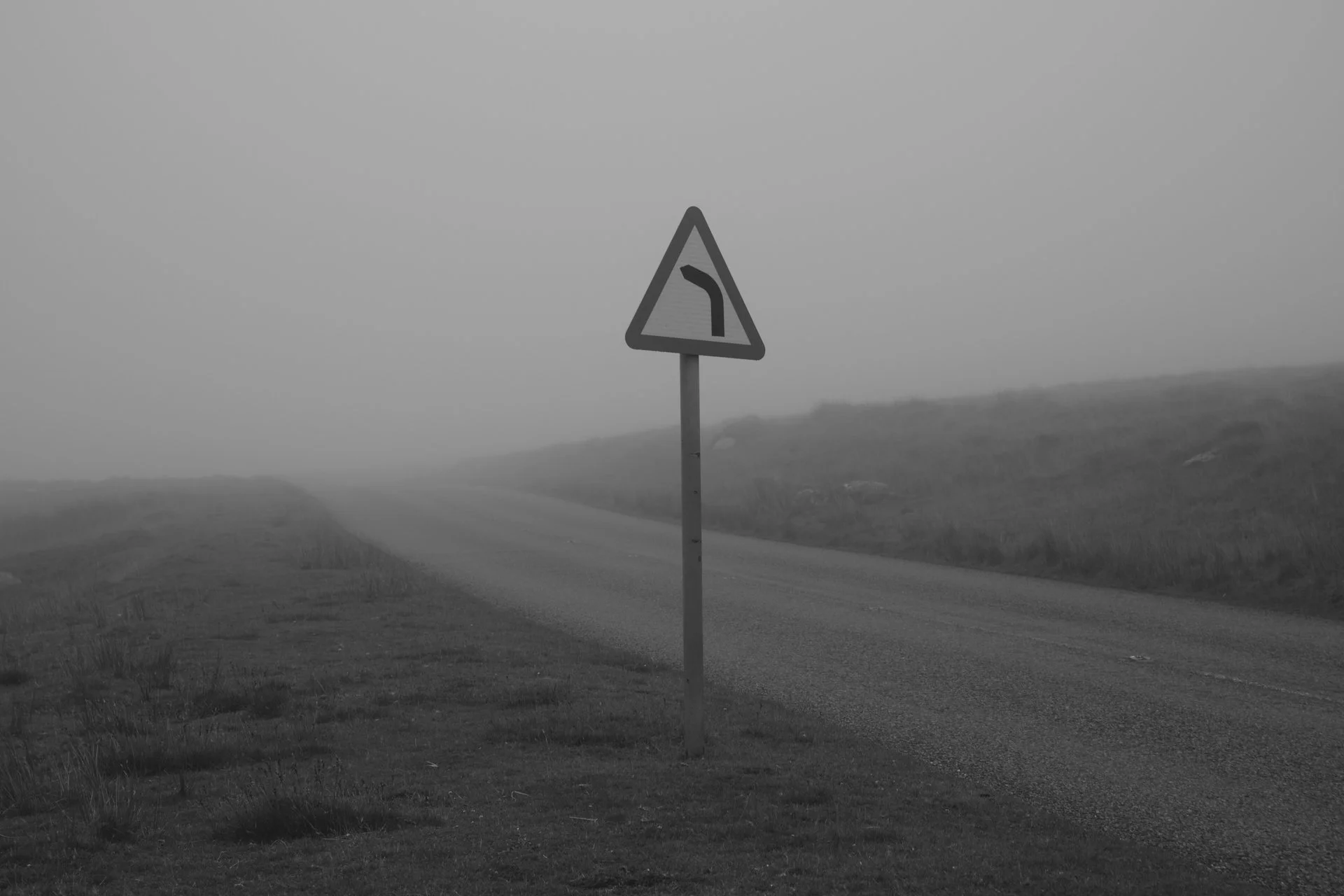 A foggy rural road with a traffic sign indicating a sharp curve ahead.