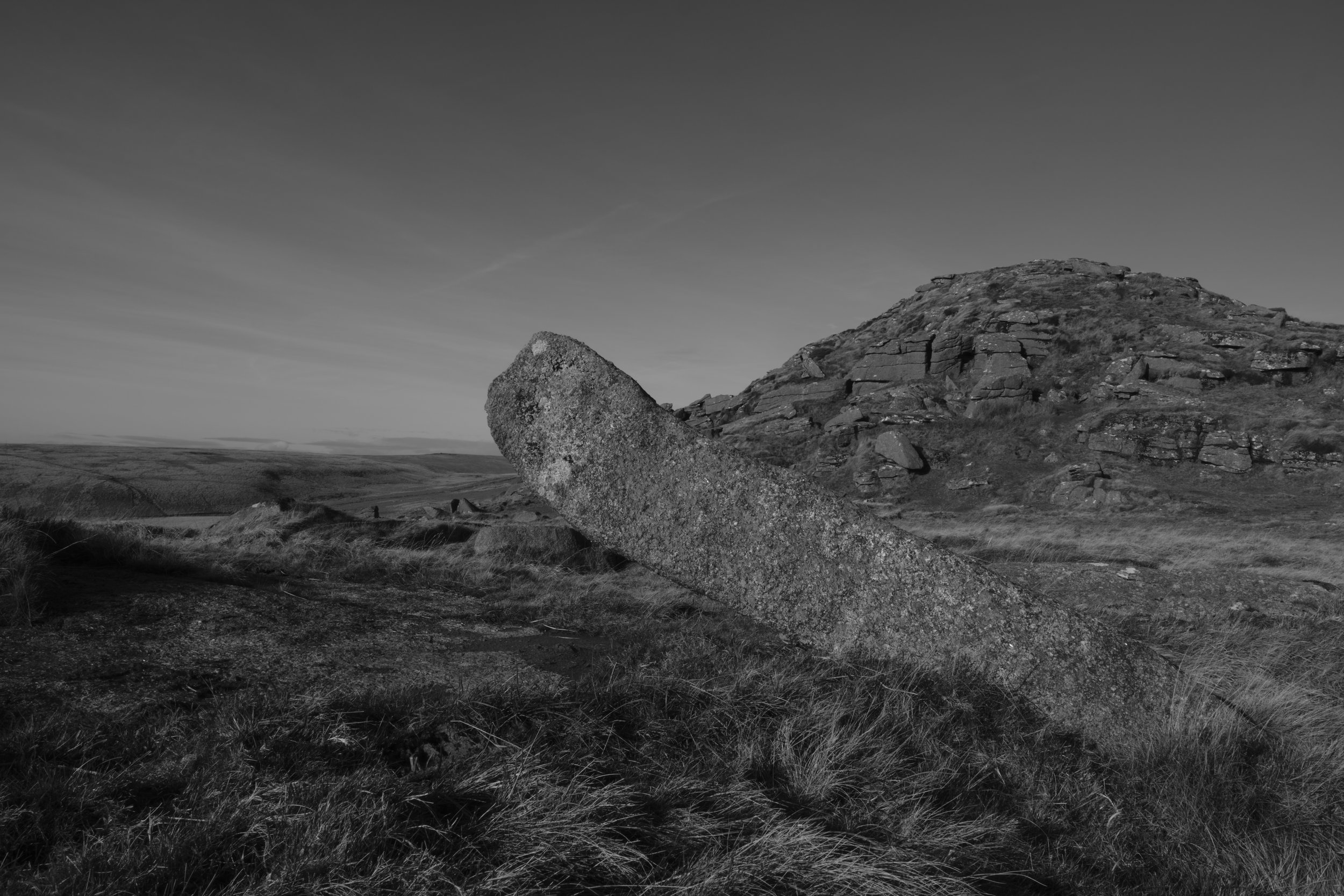 A rock sticks out of the ground with Crow's Tor visible in the background.