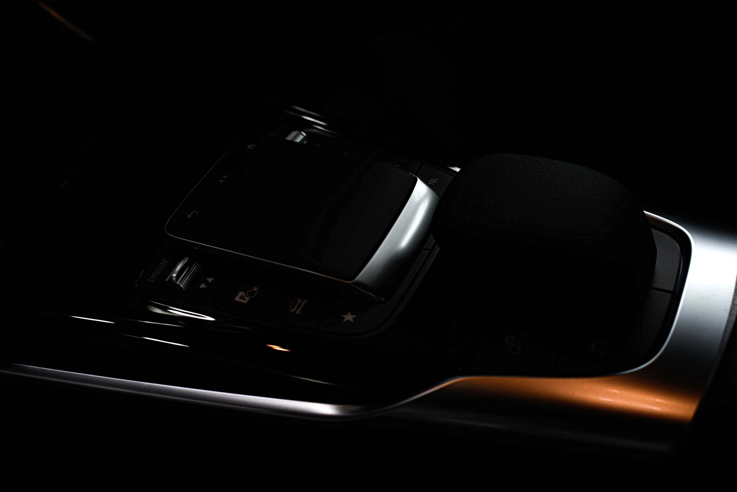 Close-up of a luxurious car interior with a sleek black and metallic silver center console. Buttons and controls are subtly illuminated in low light.