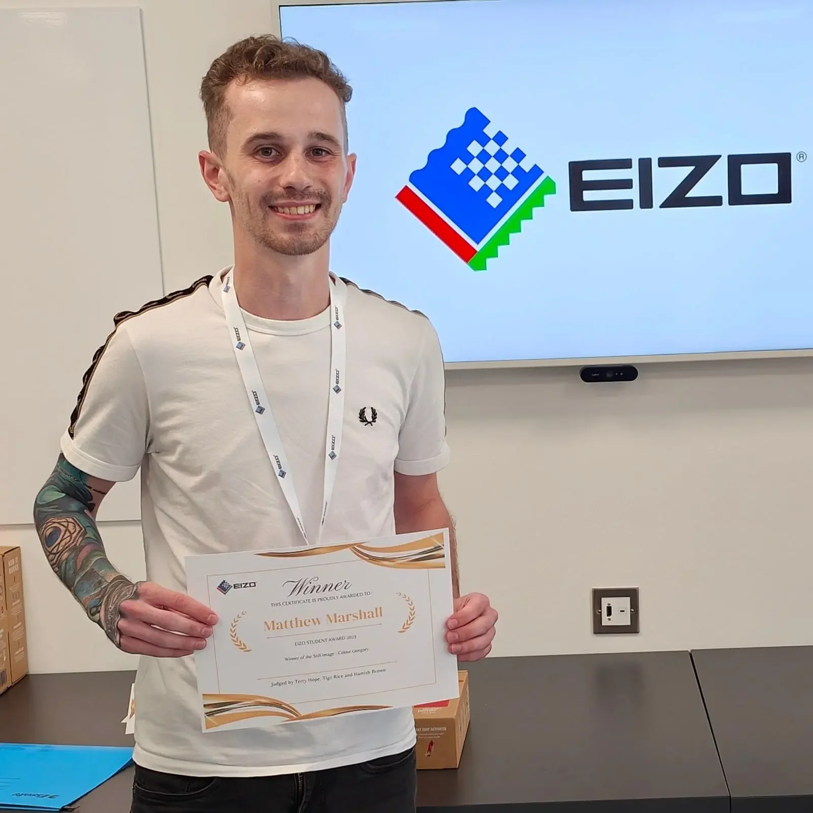 A man with a coloured tattoo sleeve hold a certificate at EIZO Headquarters in Ascot.