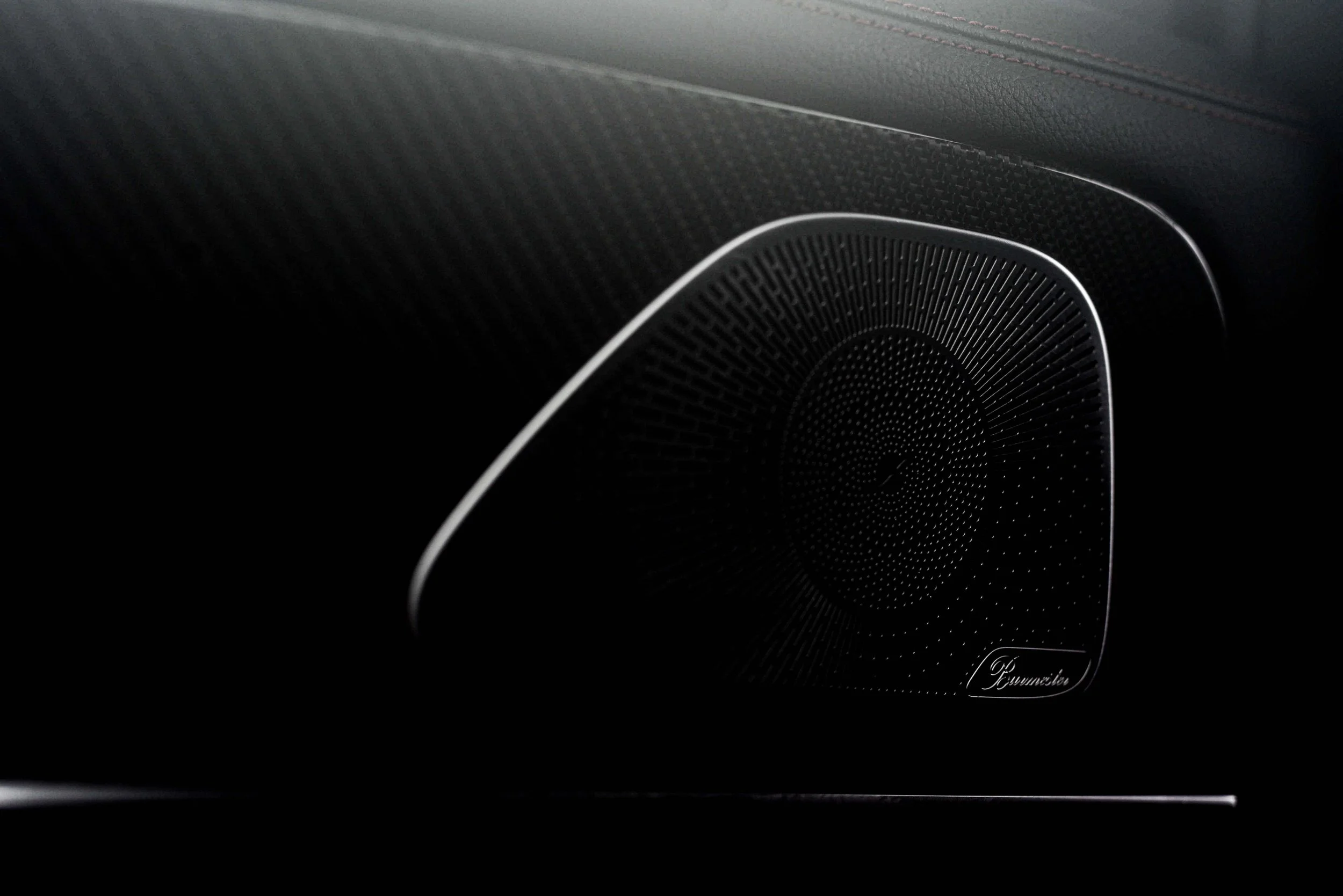 Close-up of a sleek black car speaker with intricate circular patterns and a metallic finish. The scene has a modern, sophisticated tone.