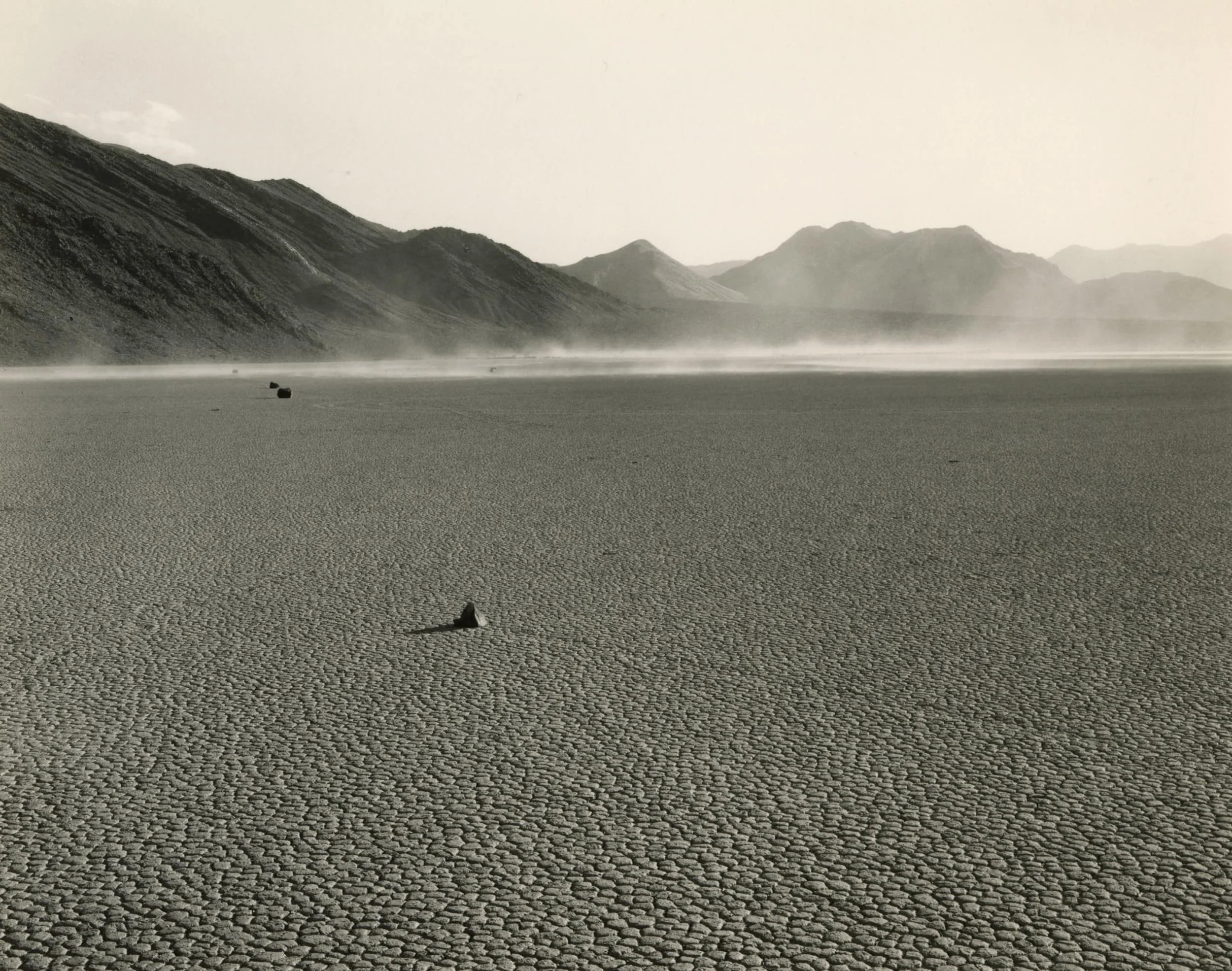 A photograph courtesy of Mark Ruwedel of a rock with mountains as a backdrop and dusty conditions.