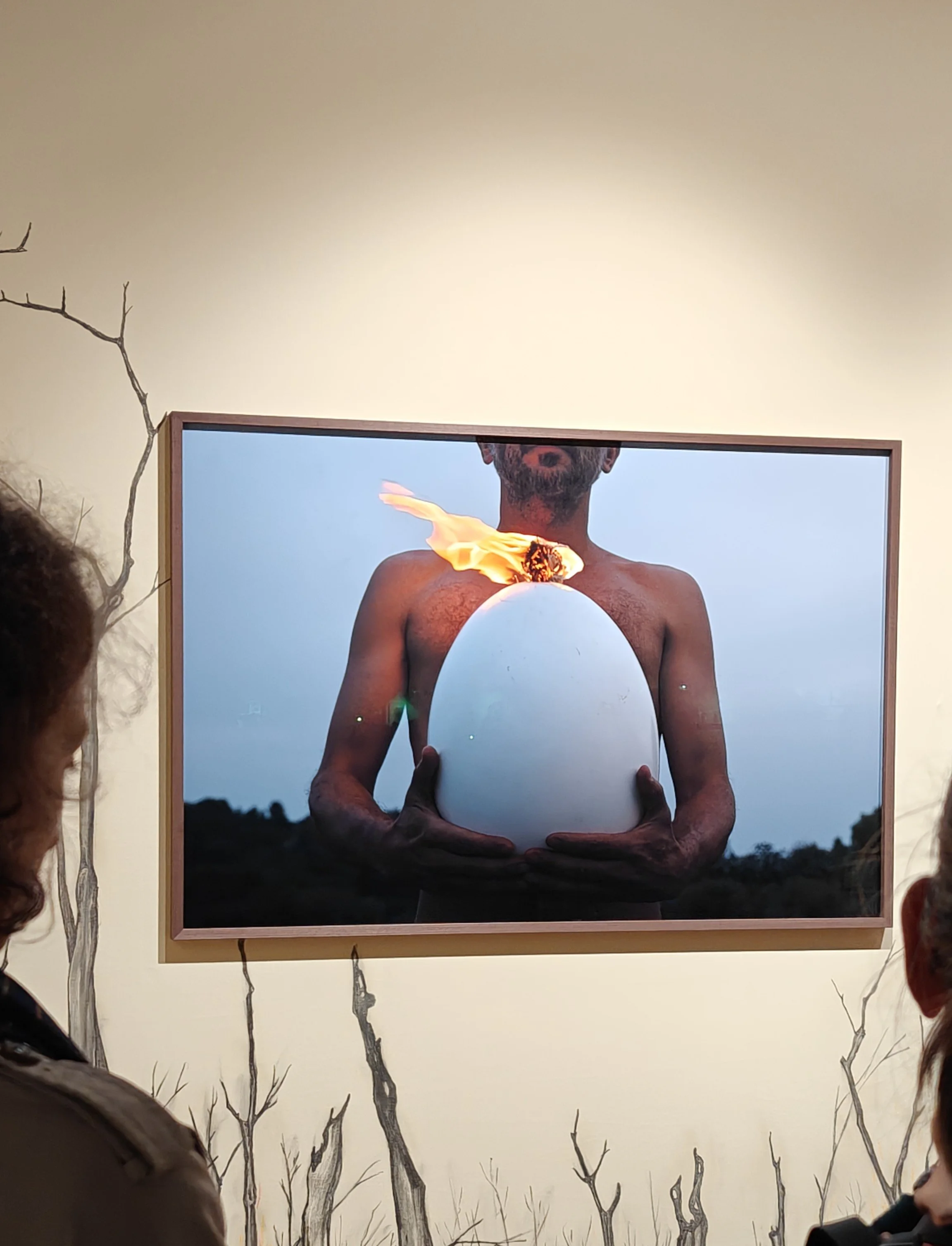 Colour photograph of Rodrigo Braga's framed photograph of a man with no shirt holding an egg with a flame on top exhibited at Paris Photo Fair 2025