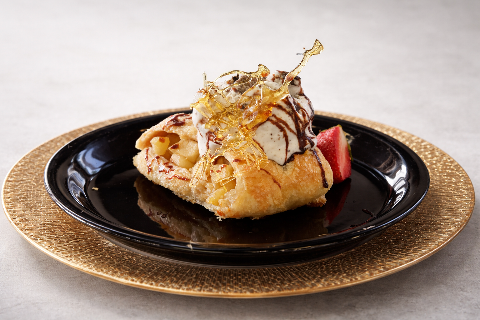 Postre con helado de vainilla, chocolate, frutos y caramelo en plato negro sobre superficie clara
