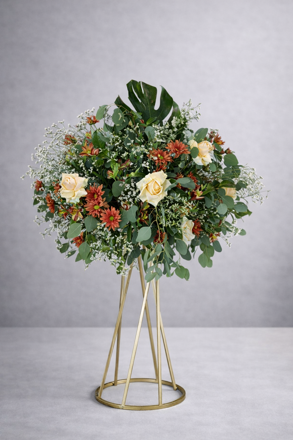 Arreglo floral con rosas blancas, pequeñas margaritas rojas y diversas hojas verdes en jarrón dorado