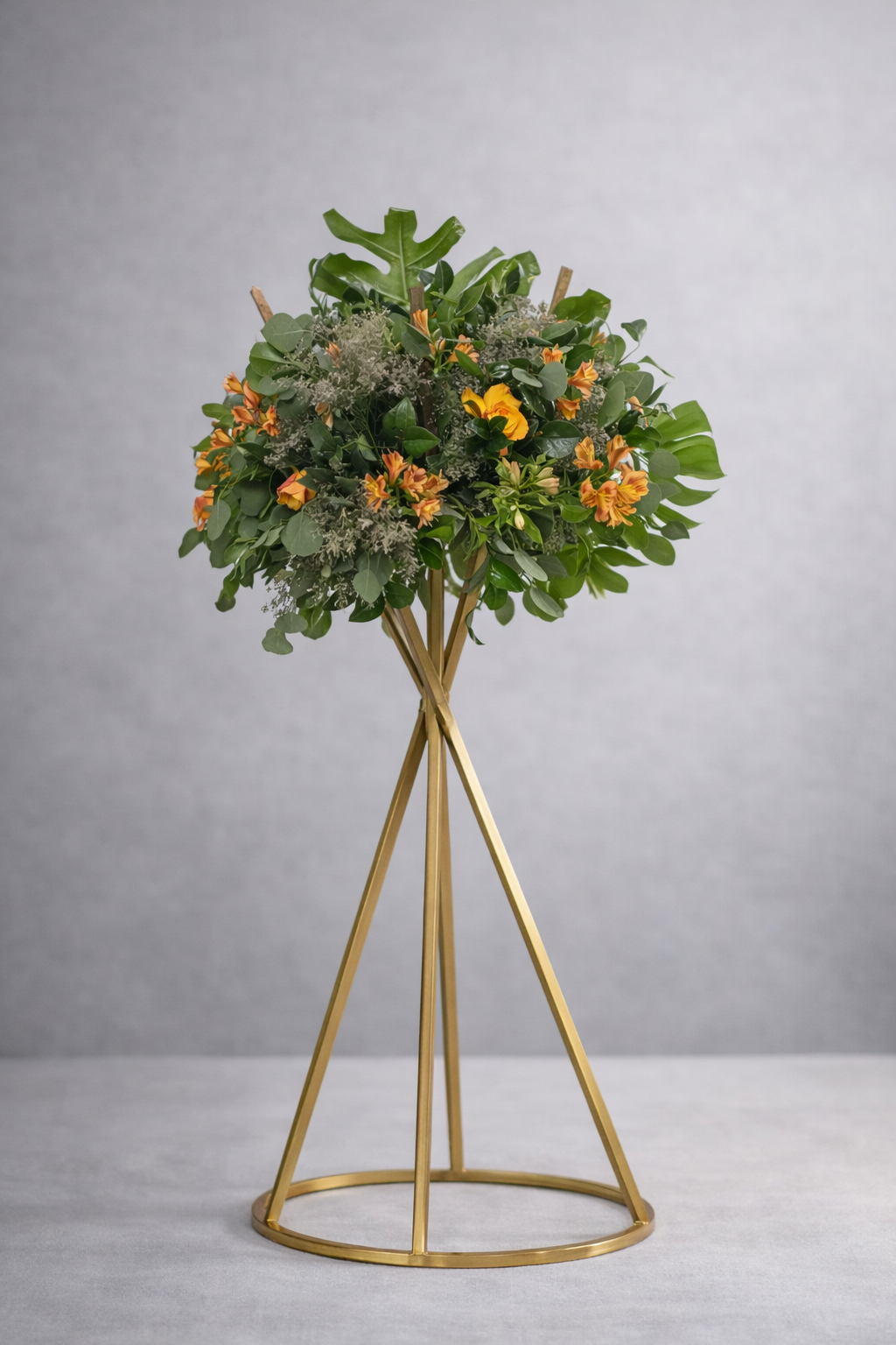 Arreglo floral con flores naranjas y verdes en base metálica dorada