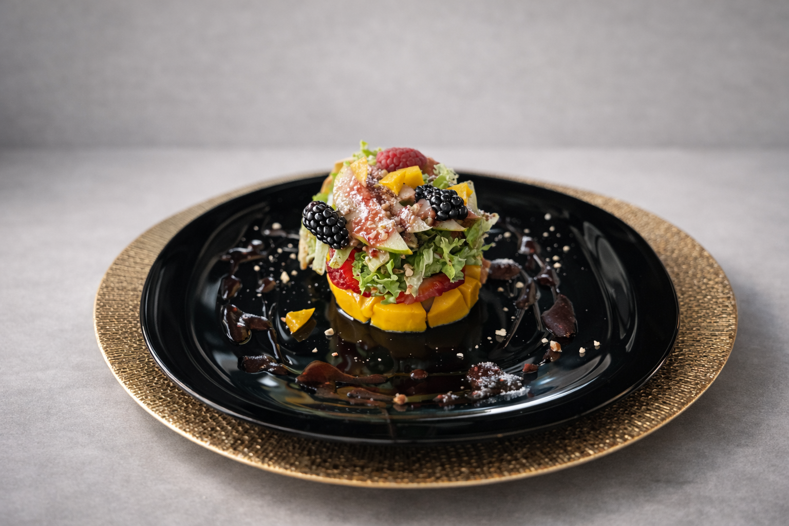 En un plato negro hay una ensalada de fruta decorada con frutas variadas como frambuesas, moras, mango, y otros ingredientes, con salsa de chocolate alrededor del plato.