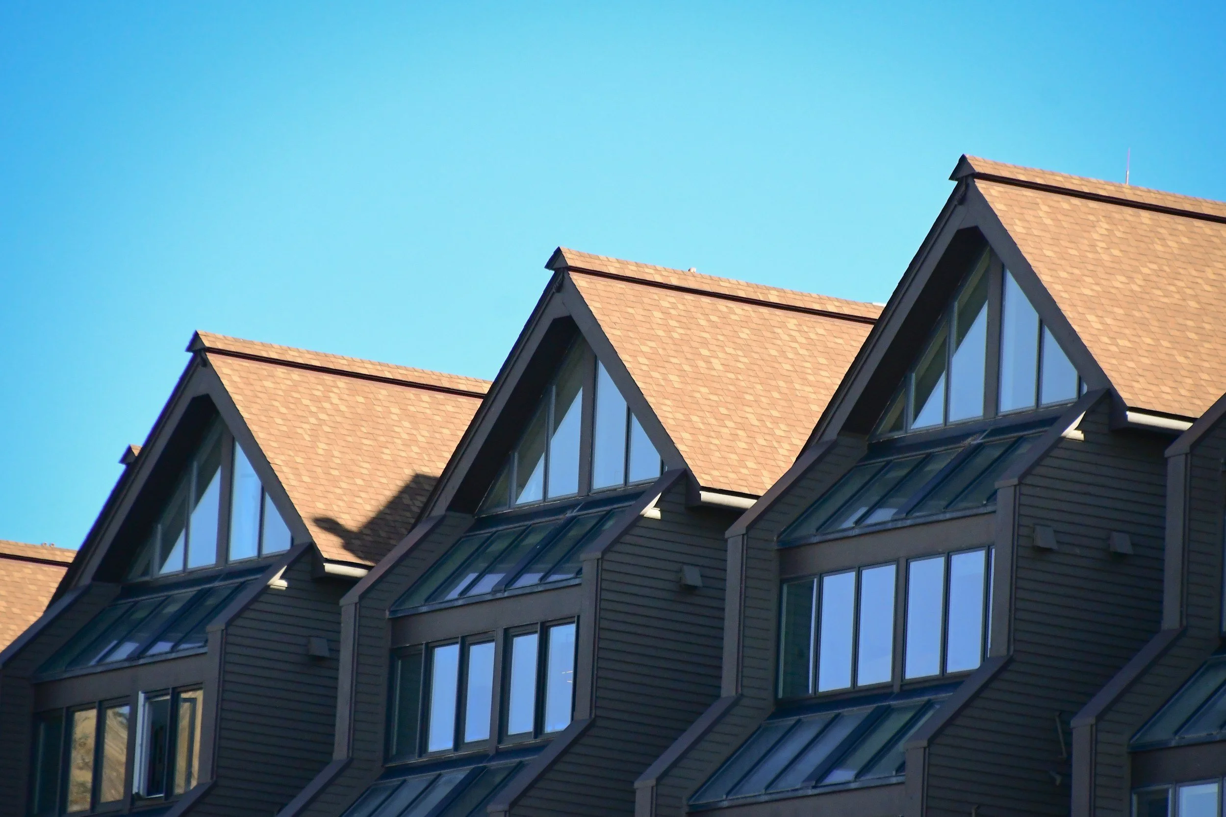 Several modern houses with sloped orange roofs and large windows reflecting the blue sky.