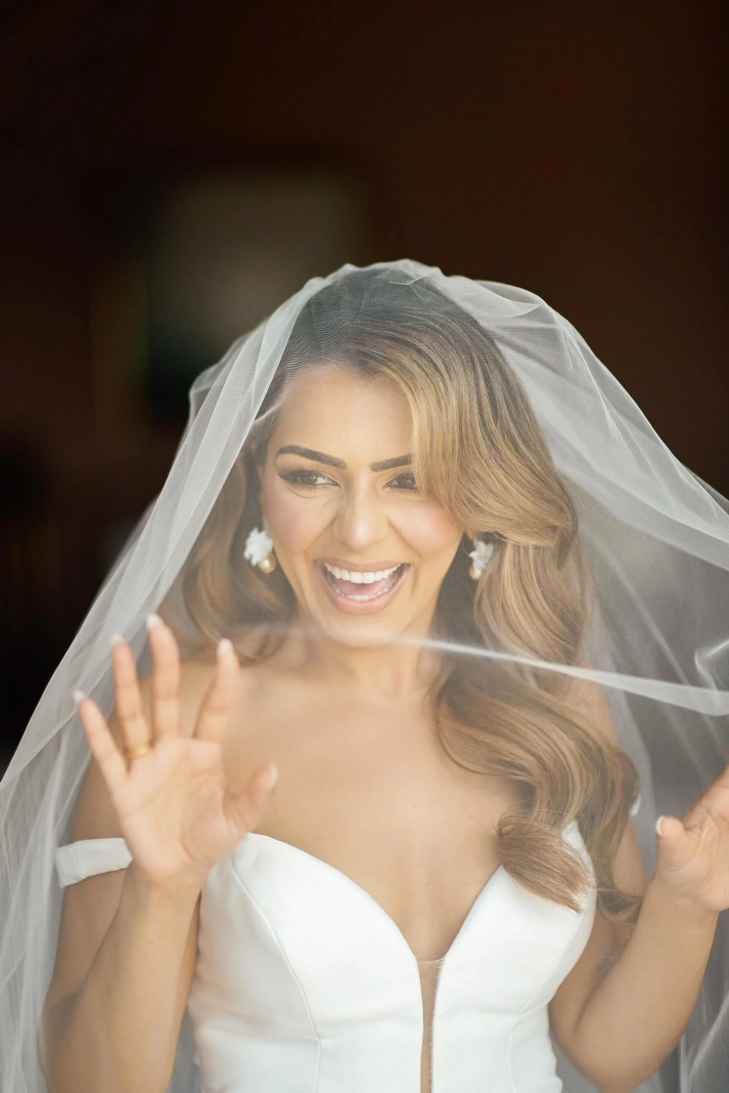 Bride with romantic soft waves at ekaterini estate Corfu,  in a wedding dress with a veil, smiling and waving.