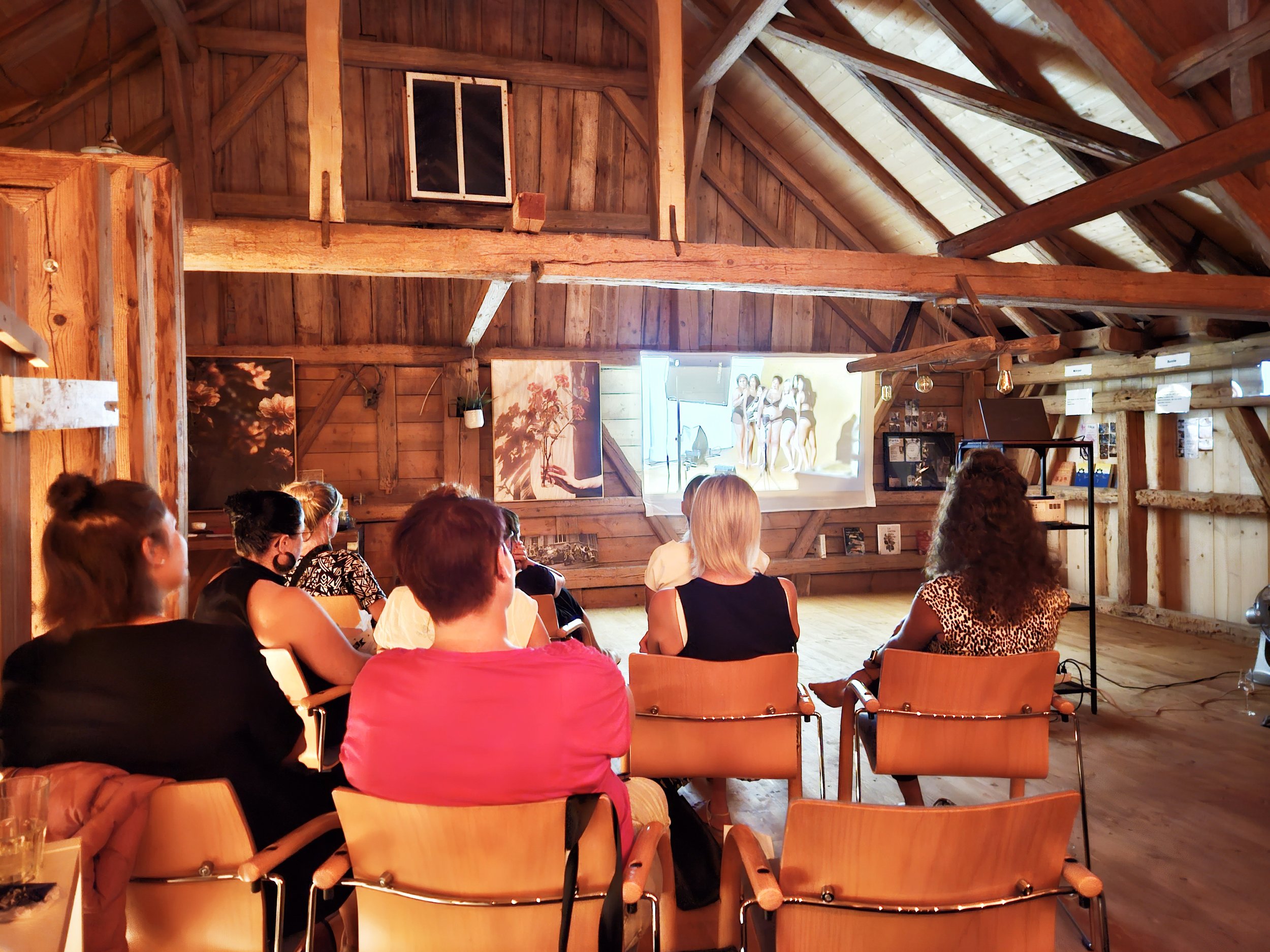 Menschen sitzen in einer schönen umgebauten Scheune und schauen einen Film oder eine Präsentation an, die auf einer Leinwand im Raum gezeigt wird.