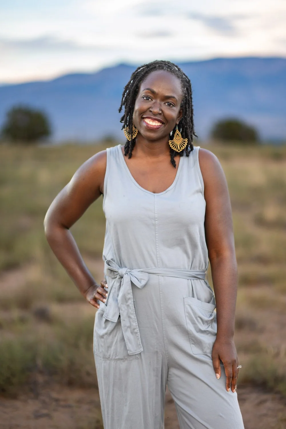 Portrait of a smiling Black woman with her hand on her hip, standing outside in front of a mountain range